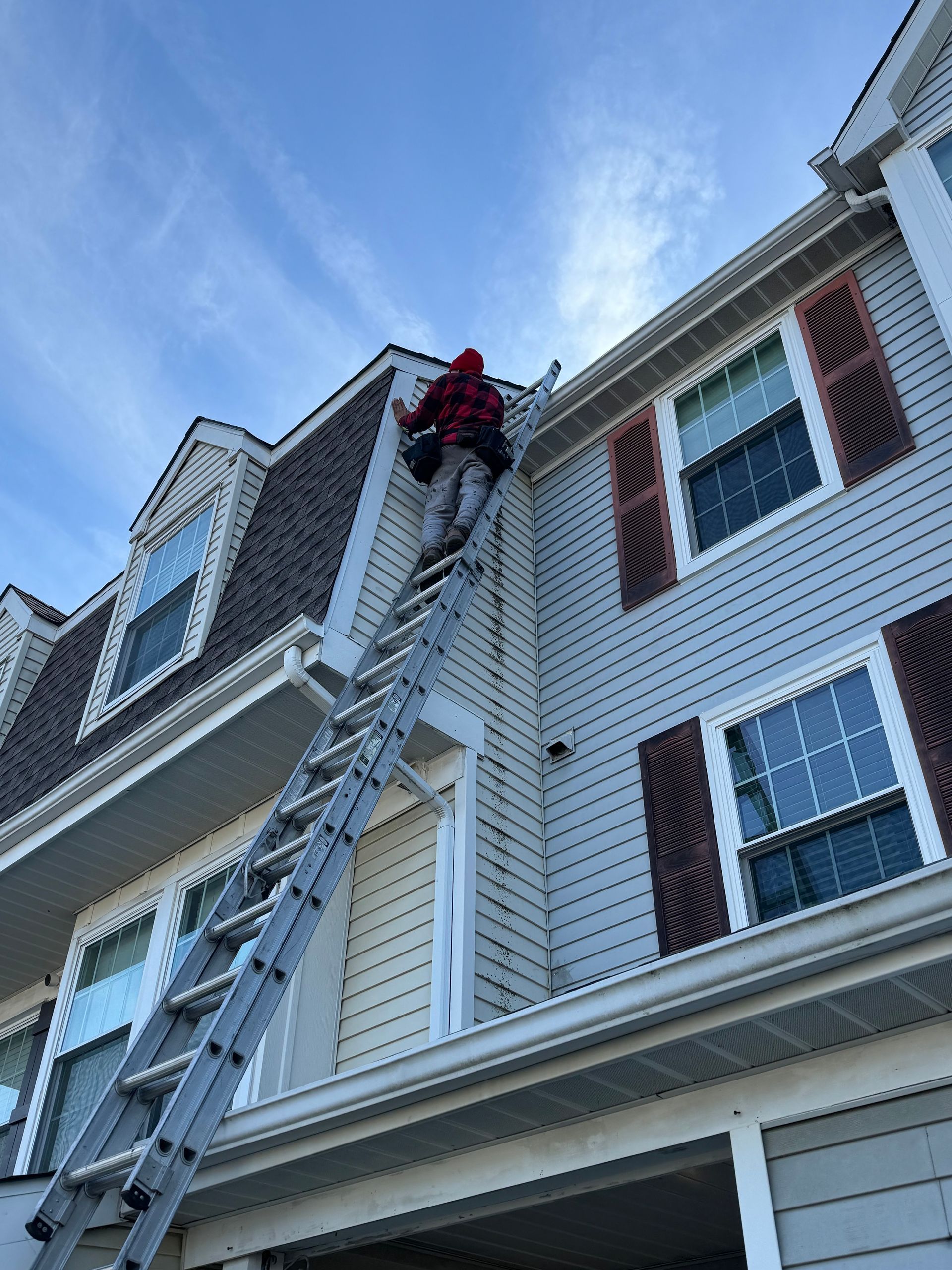 Worker on a ladder repairing the siding of a white townhouse under a blue sky