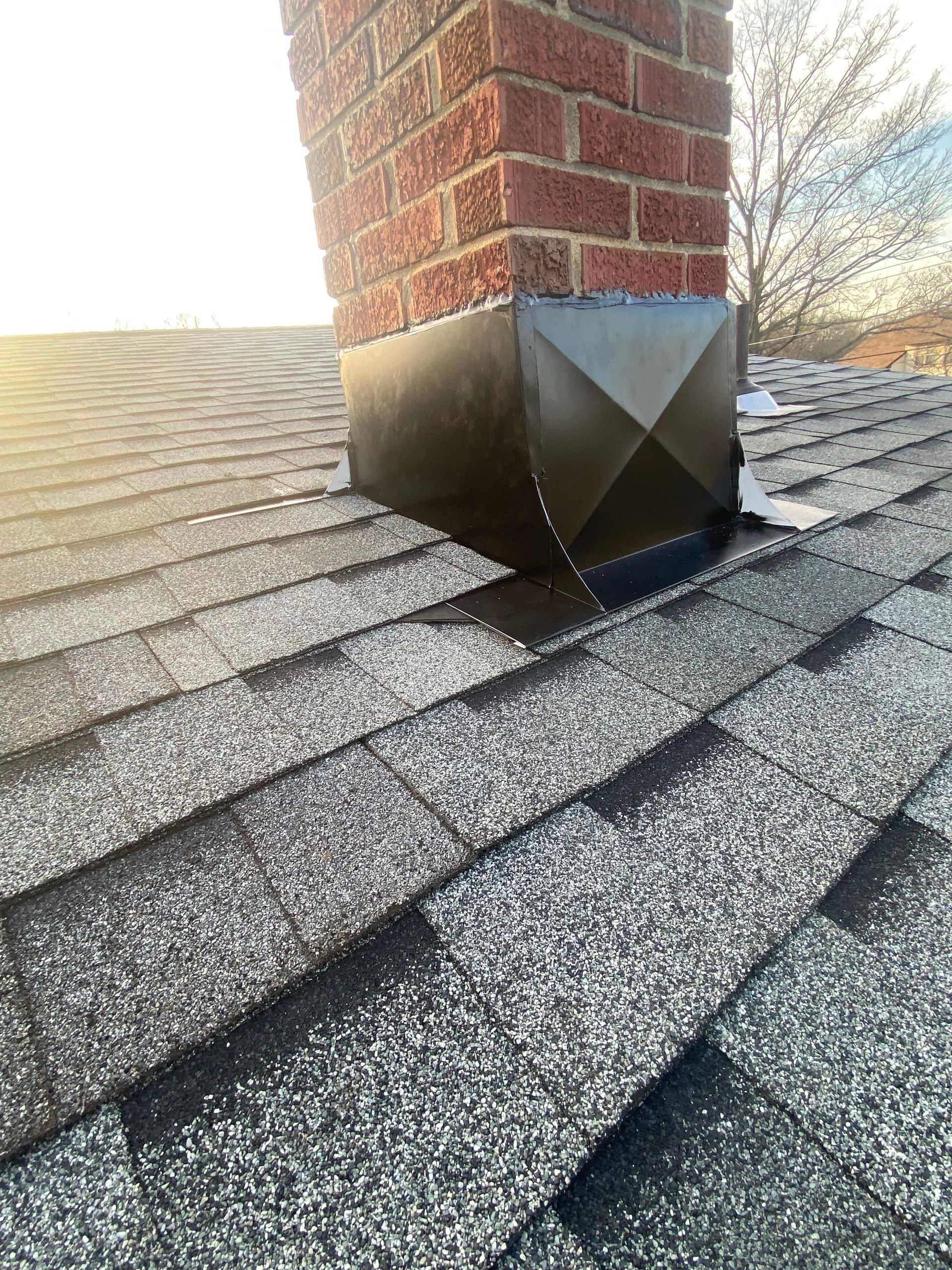 Brick chimney with a black metal flashing on a gray shingle roof.