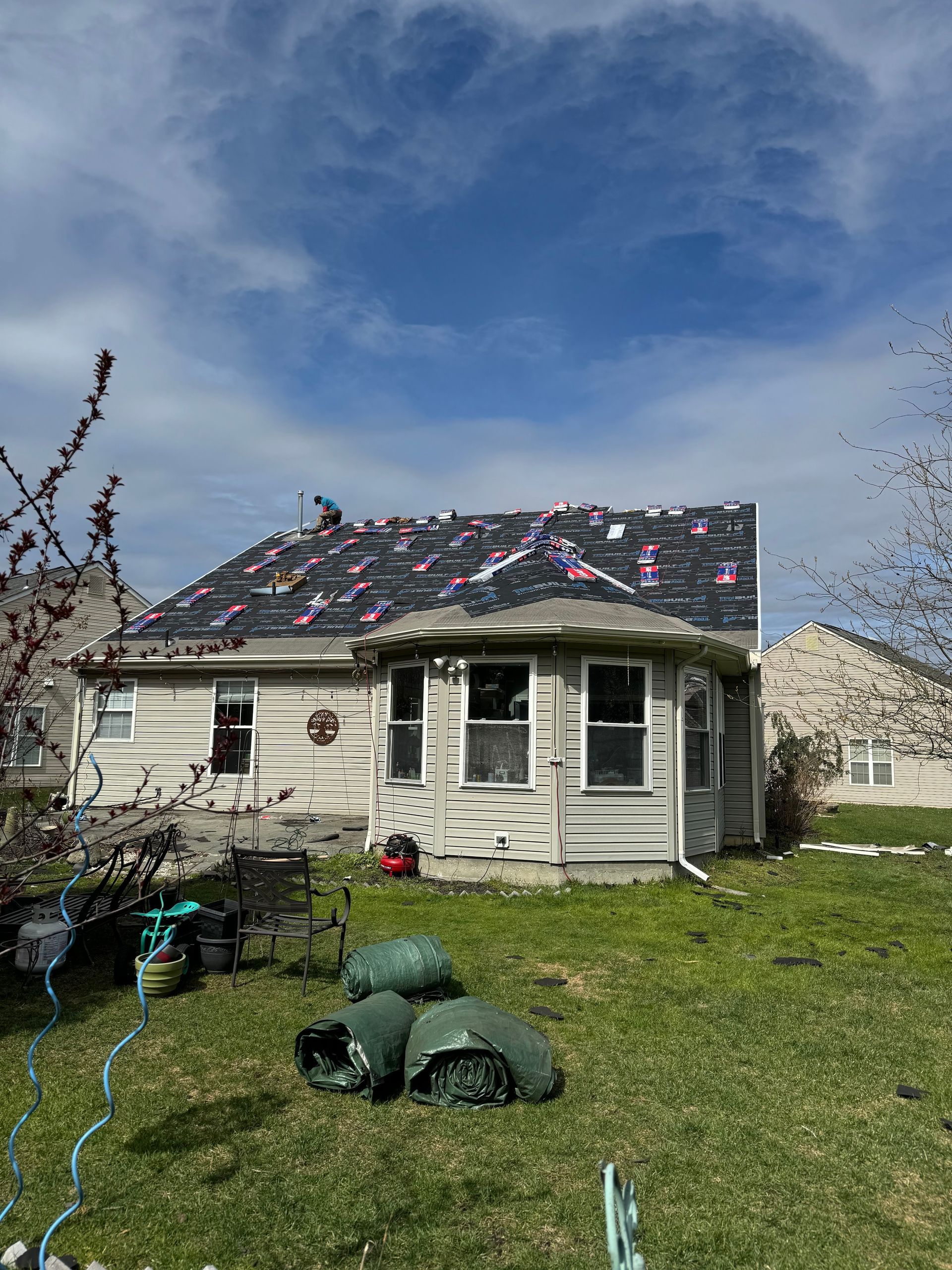 Small house with storm damage on the roof, yard littered with debris under a cloudy sky.