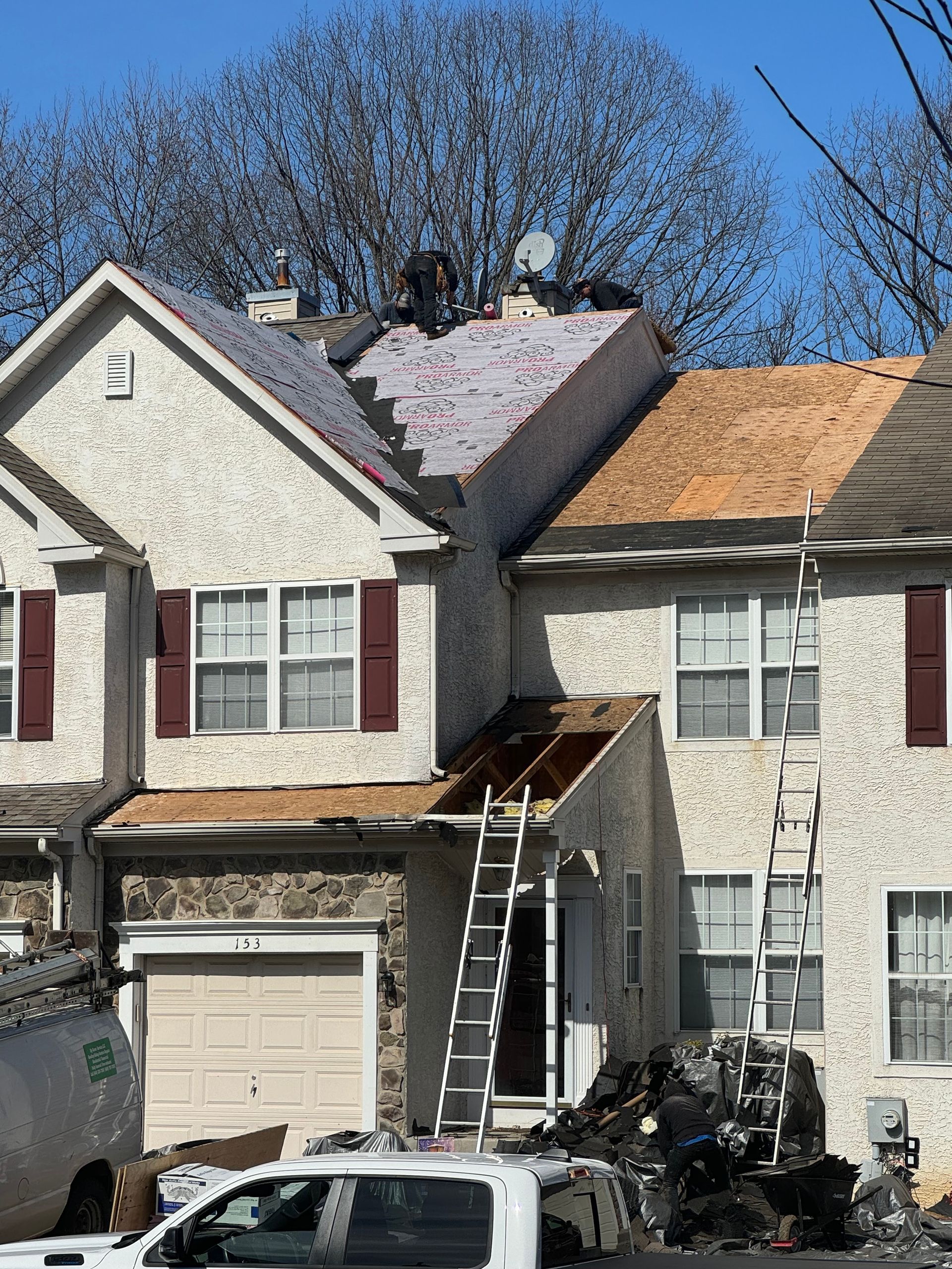 Damaged house with fire-scorched roof, ladder on front porch, and debris in driveway