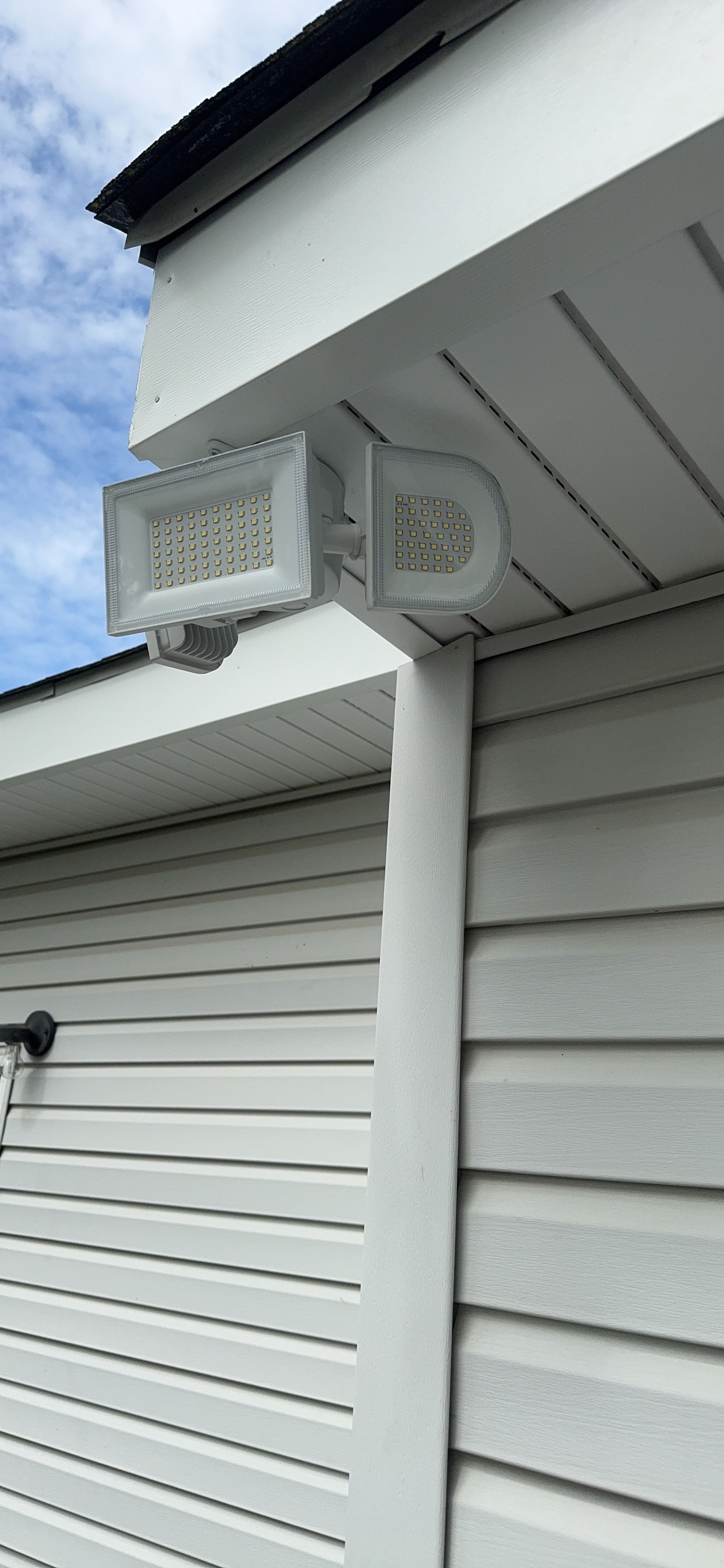 House exterior with a wall-mounted security light under the eaves beside white siding and blue sky