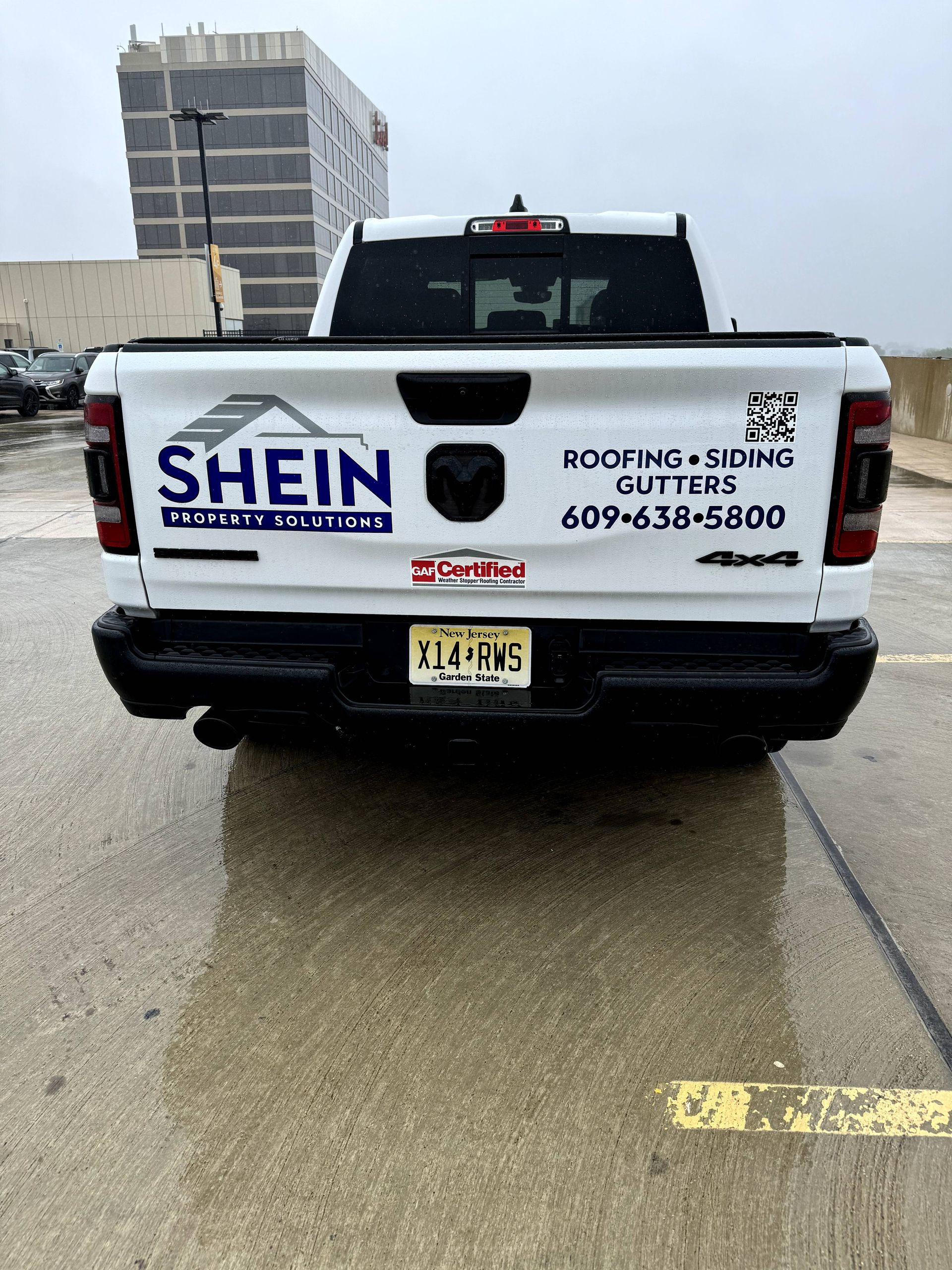 White SHEIN Roofing & Siding pickup truck parked on wet pavement in a lot