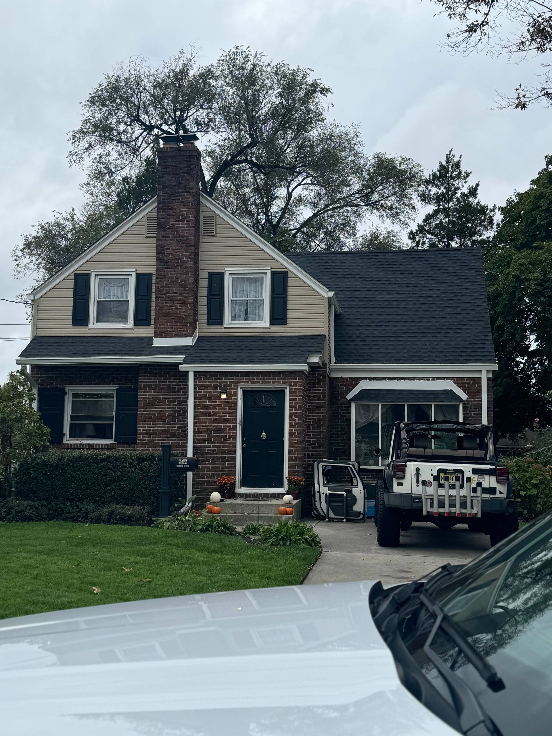 Brick house with white trim and black roof, a Jeep parked in the driveway, and a green lawn.