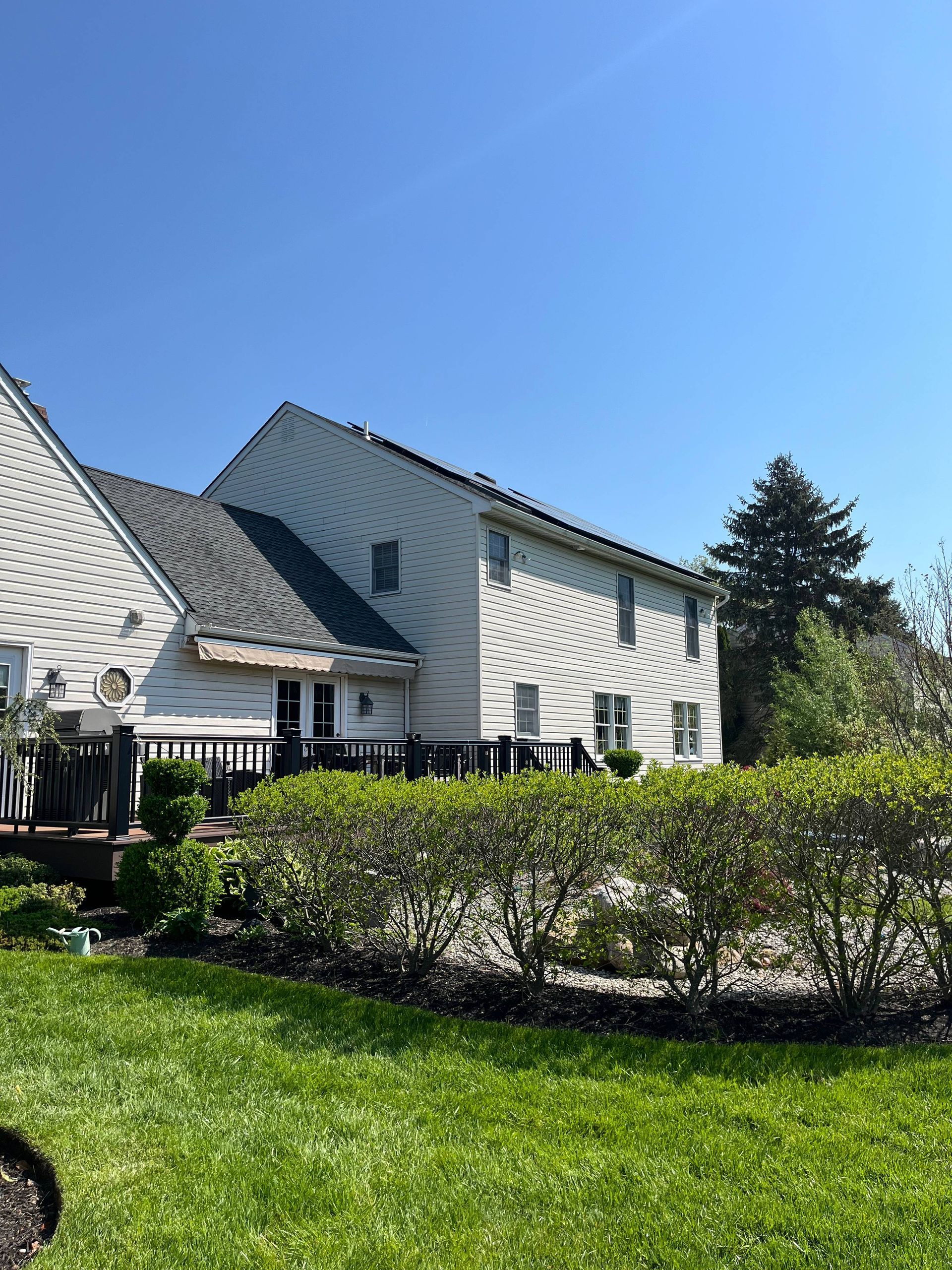 Suburban house with white siding, green lawn, trimmed hedges, and clear blue sky