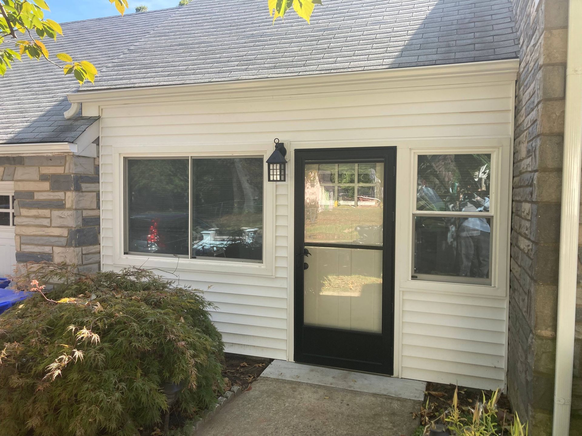 Front entrance of a house with white siding, black door, windows, and a small porch light.