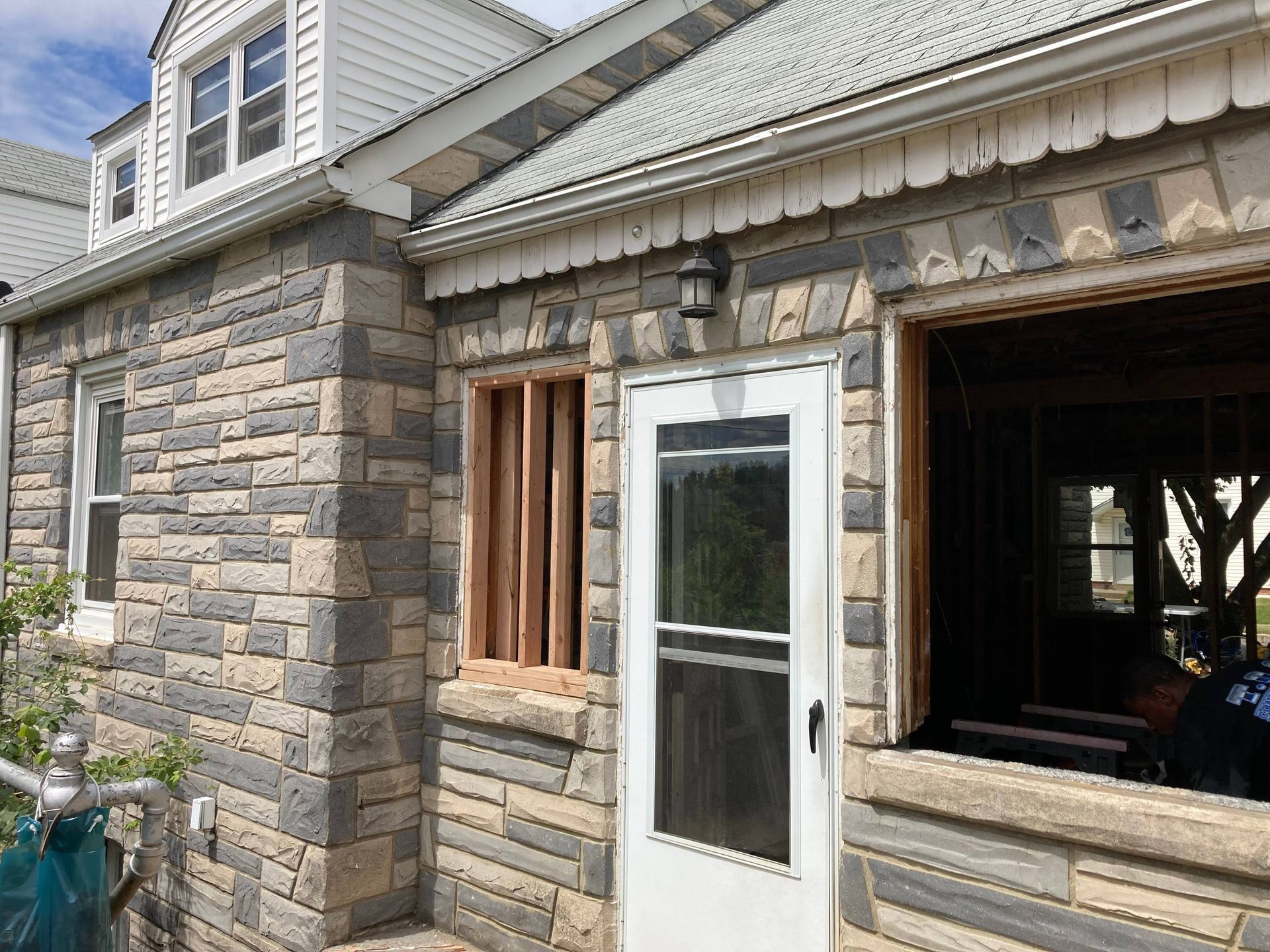 Stone house exterior with a white door, open window, and gray shingle siding