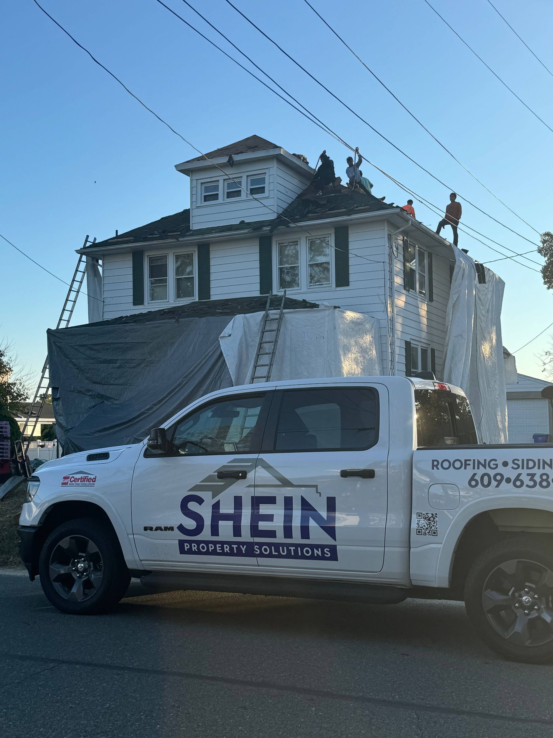 White SHEIN pickup truck parked by a tarp-covered house under power lines at dusk