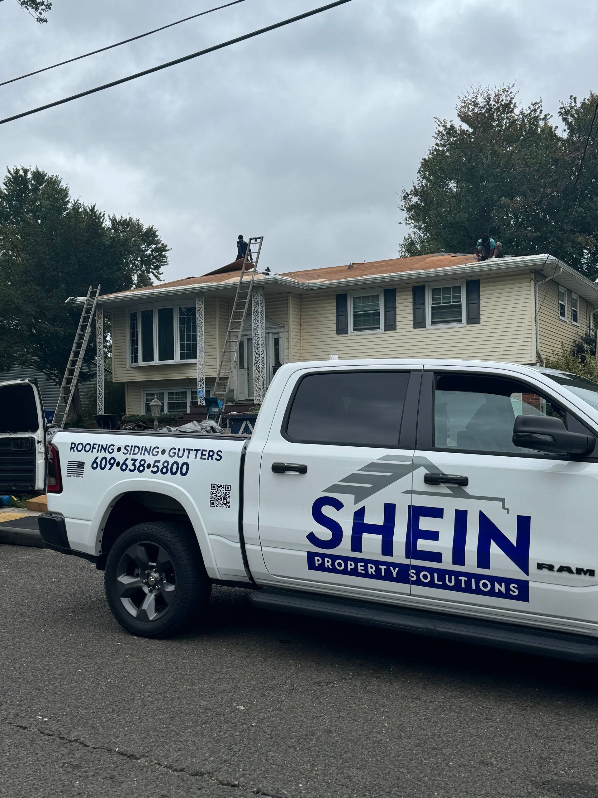 SHEIN Energy Solutions truck parked by a smoke-damaged house with workers on the roof