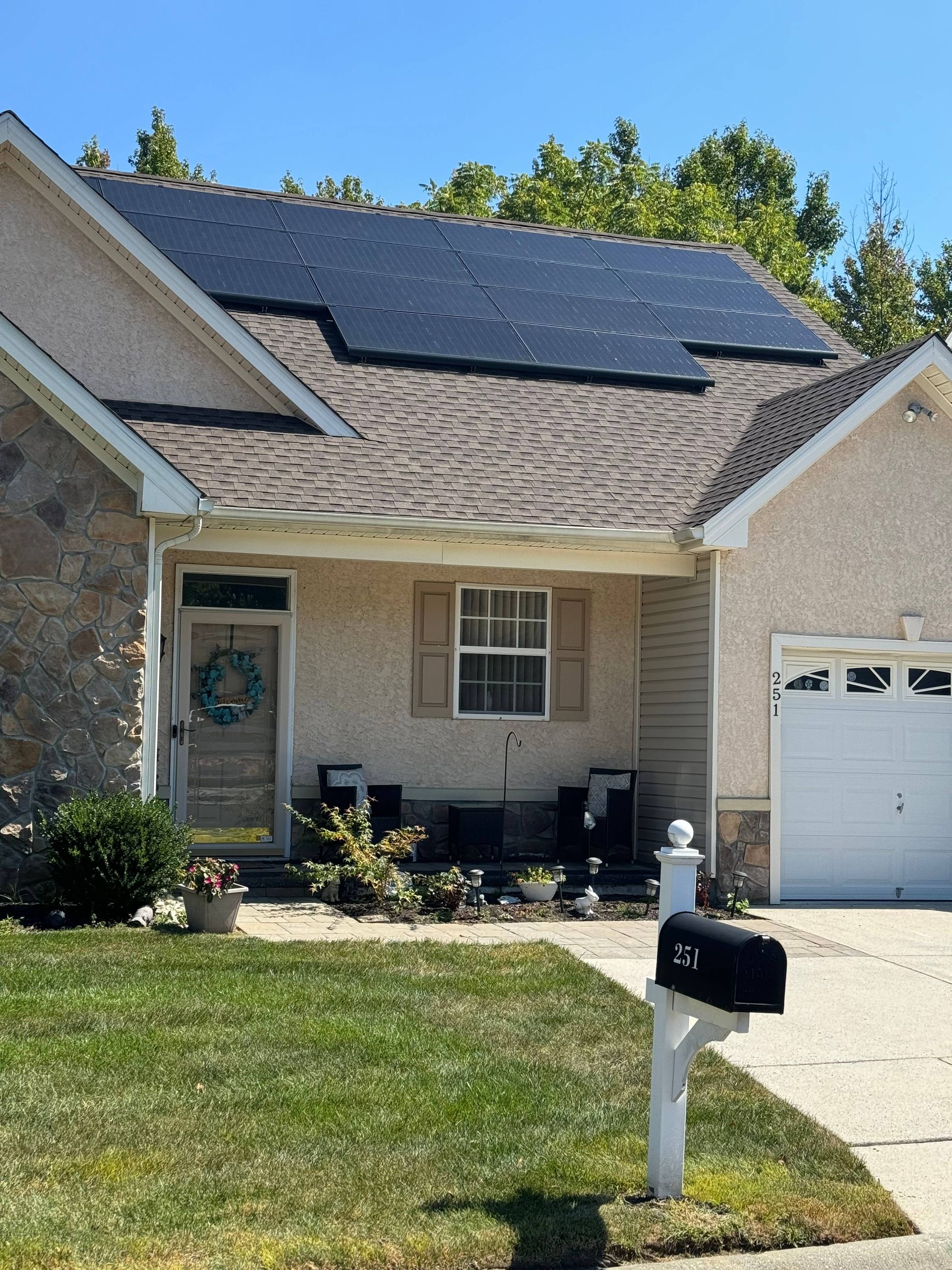 Suburban house with solar panels on the roof, front porch, garage, and a mailbox by the driveway