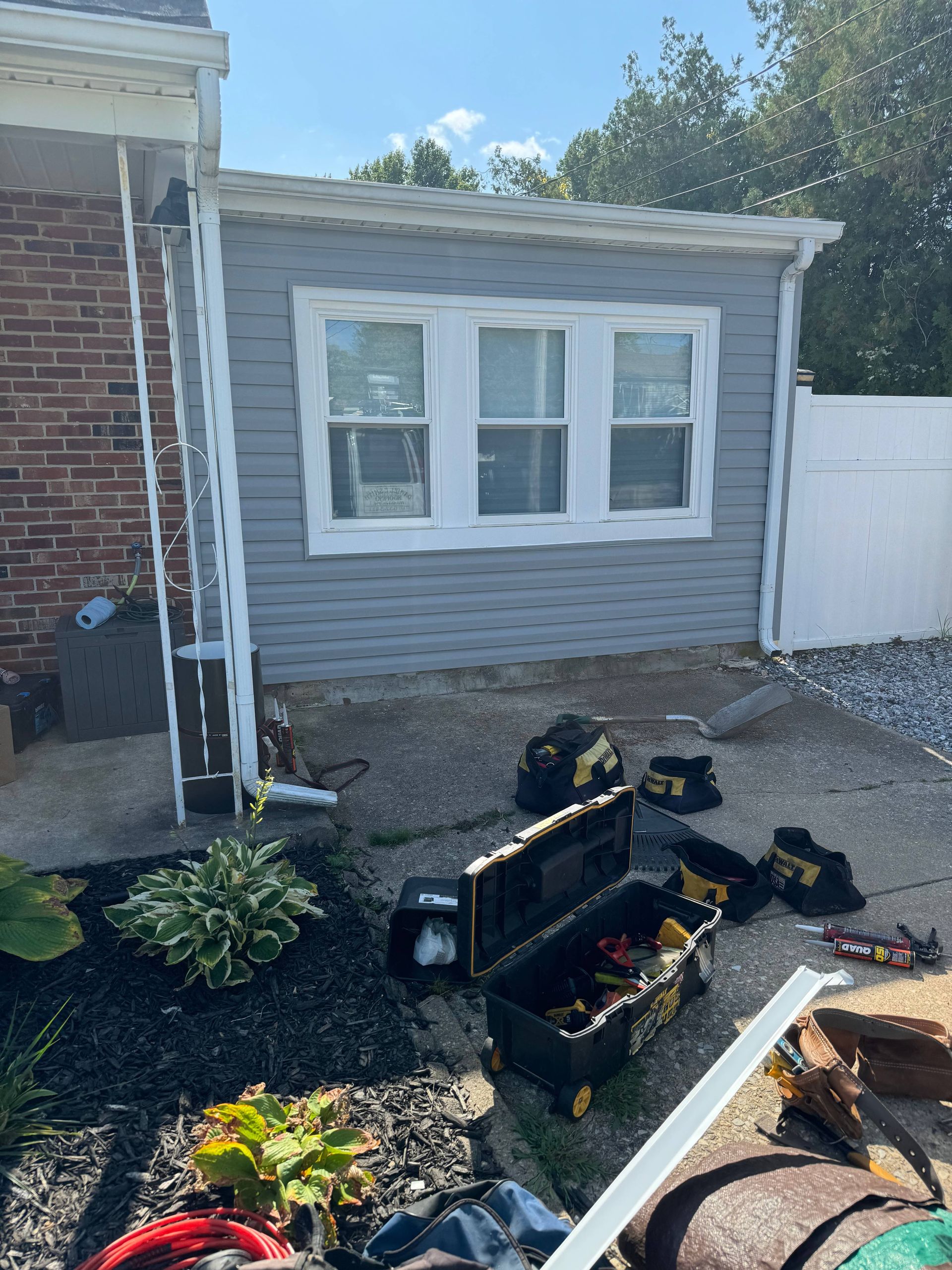 Backyard patio with gray siding, window planter work, black mulch, and a shovel on the ground
