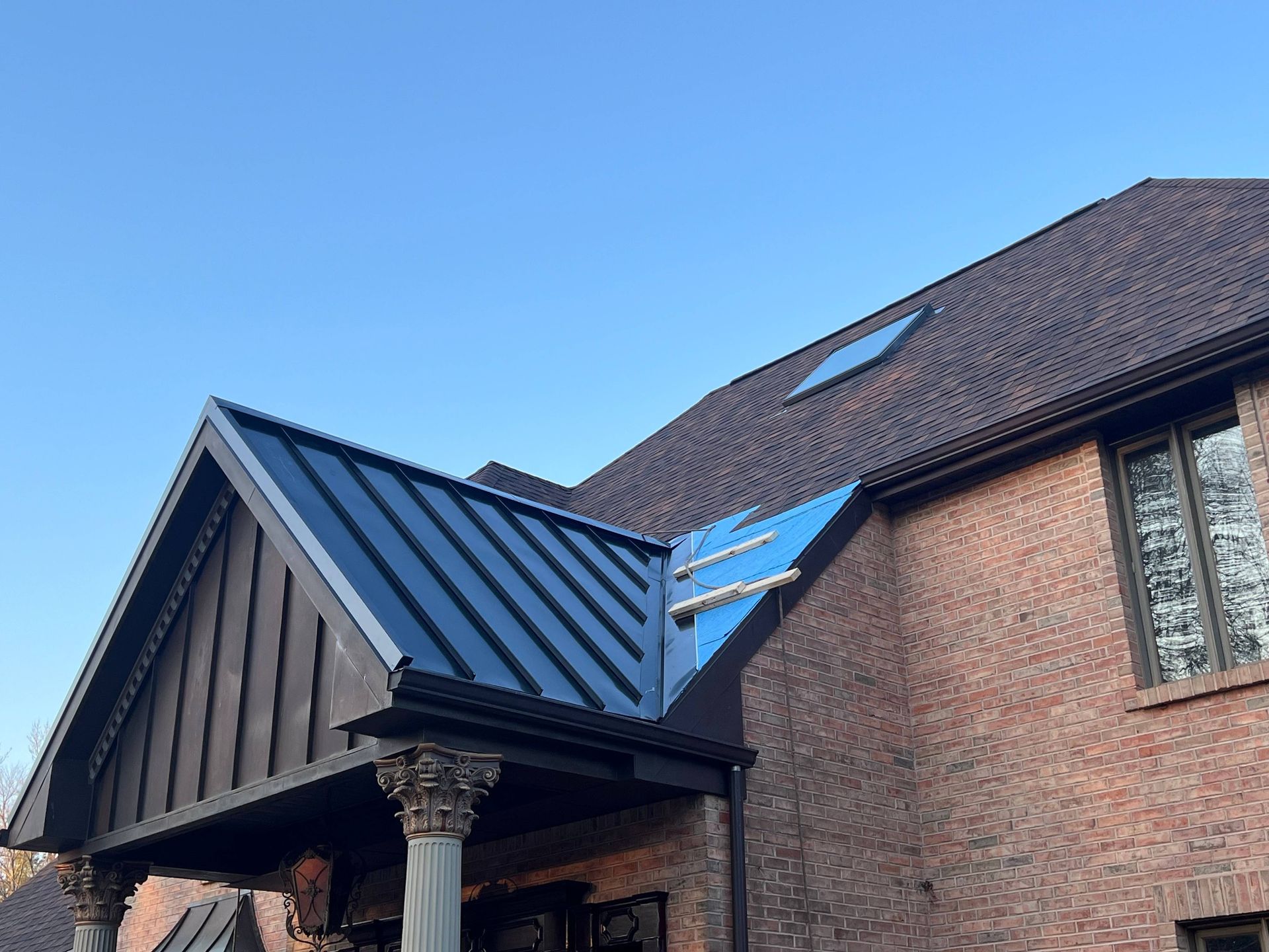Brick house with dark blue metal roof and dormer windows under a clear blue sky