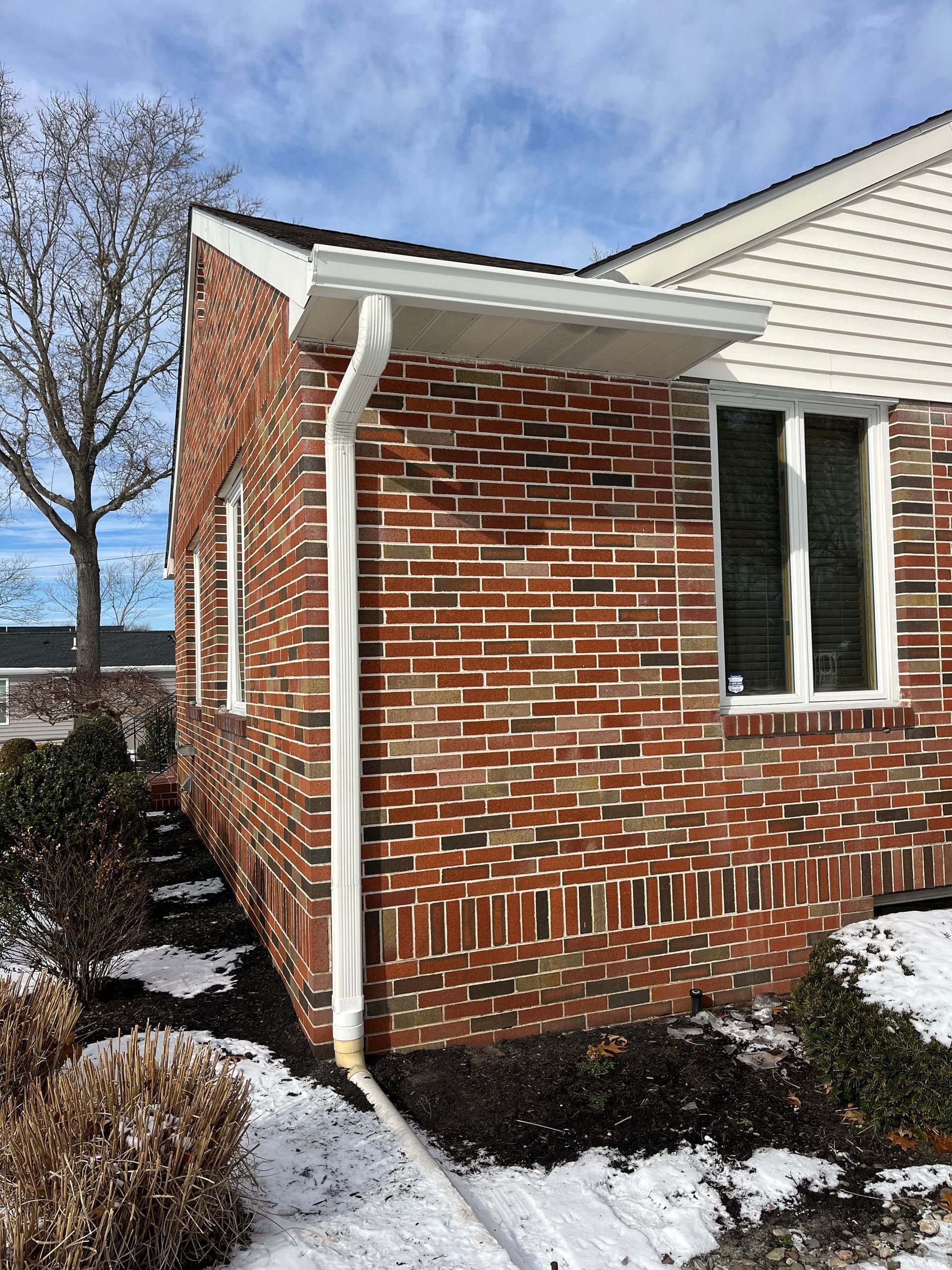 Brick house exterior with white siding, snowy ground, and a window by the corner.