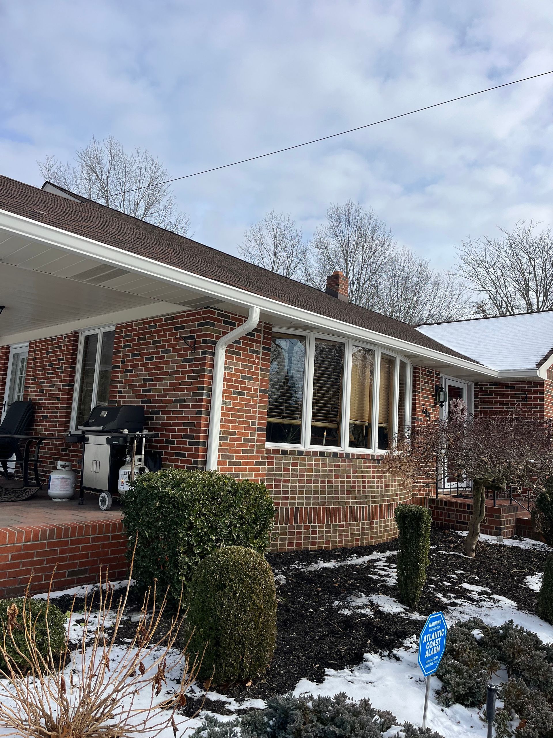 Snowy brick house exterior with a covered porch, windows, and shrubs in front