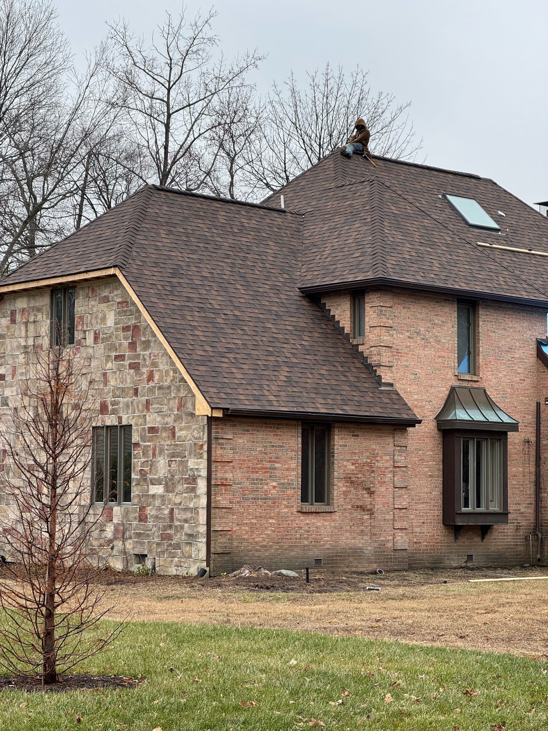 Stone and brick house with dark roof and skylight, viewed from the side in a grassy yard.