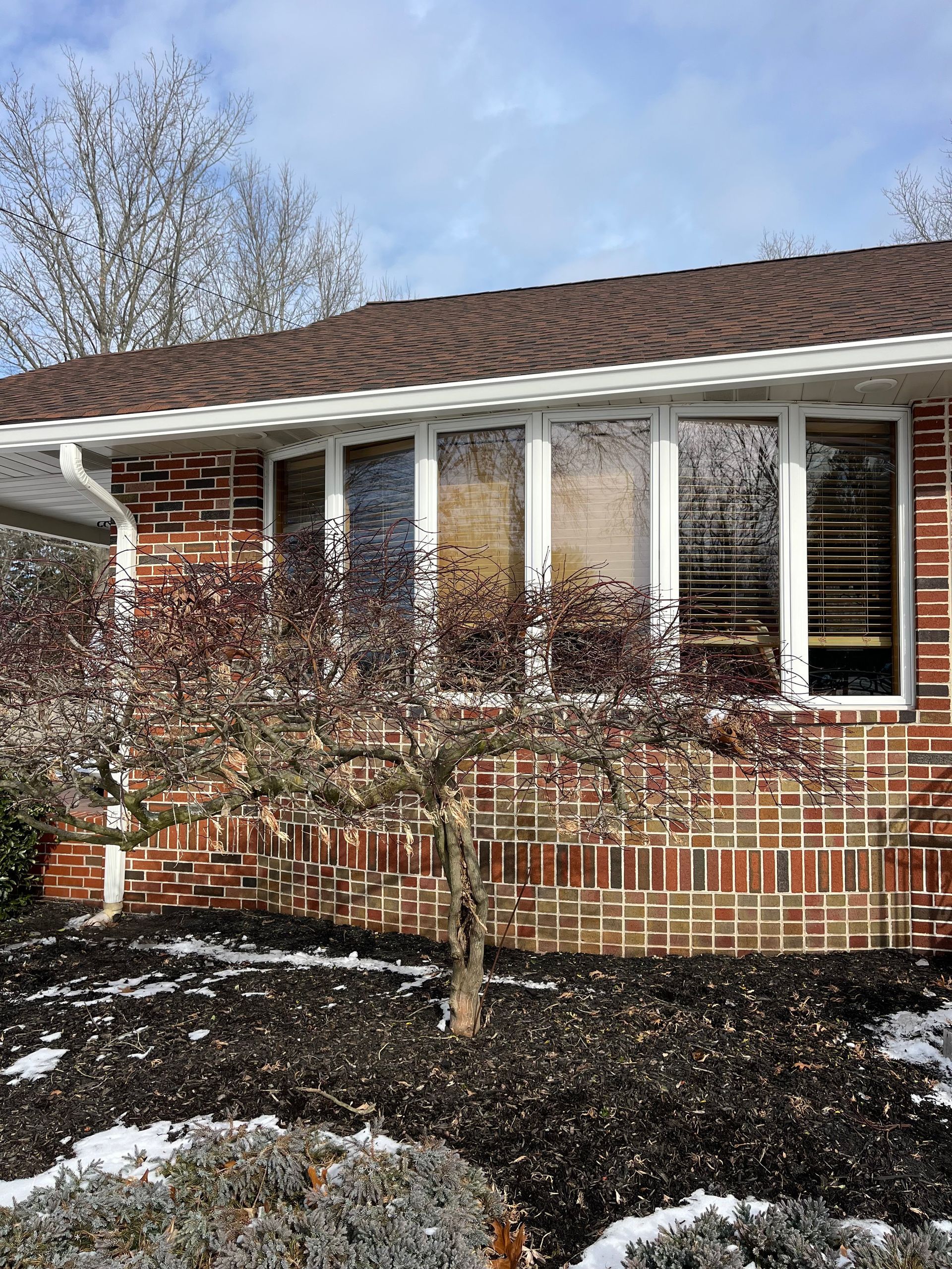 Single-story brick house with white porch columns and snow in the yard, seen in winter.