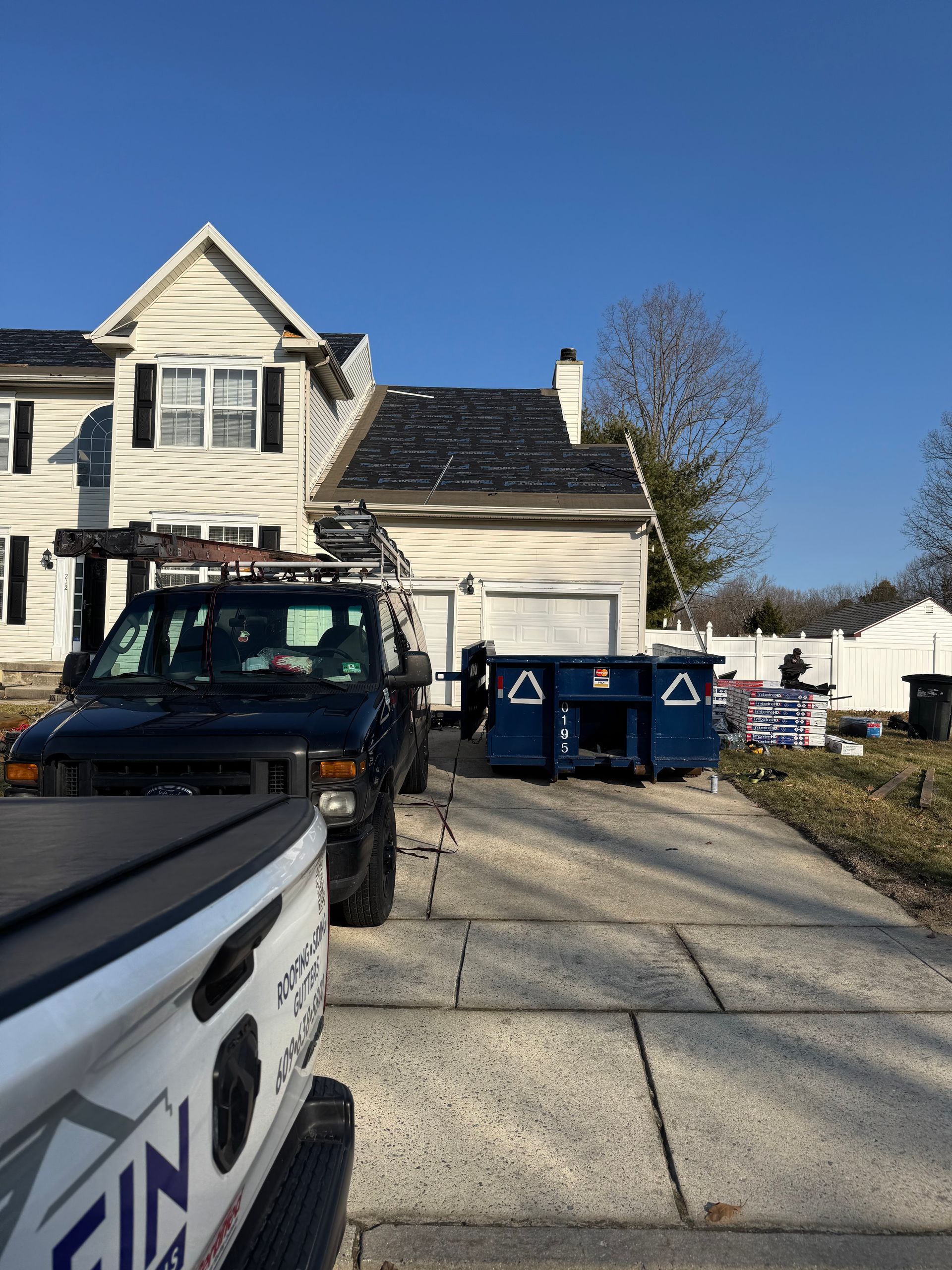 House exterior with a pickup truck and blue dumpsters in the driveway on a sunny day