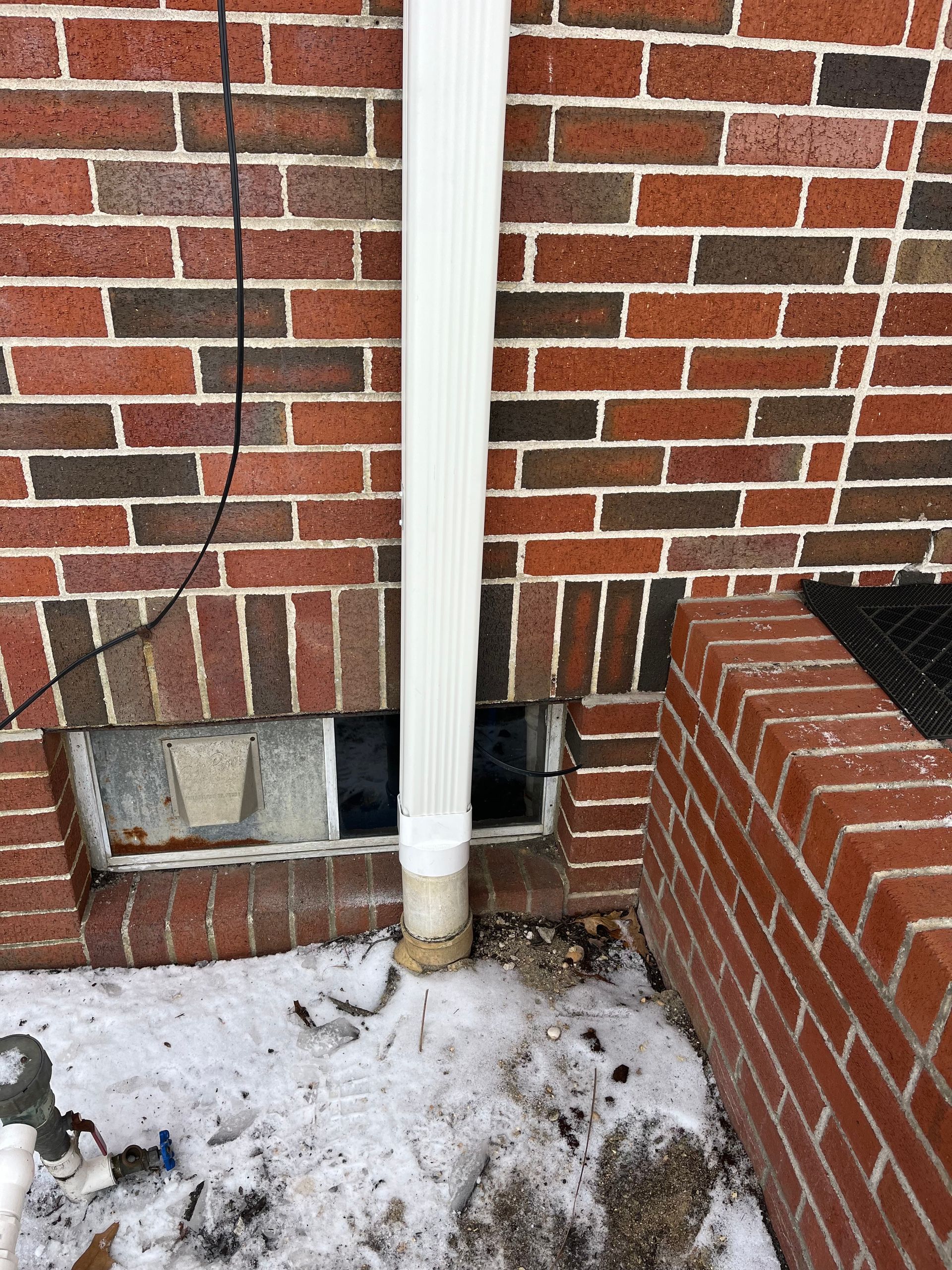 Brick house exterior with basement windows, a downspout, and snow on the ground.