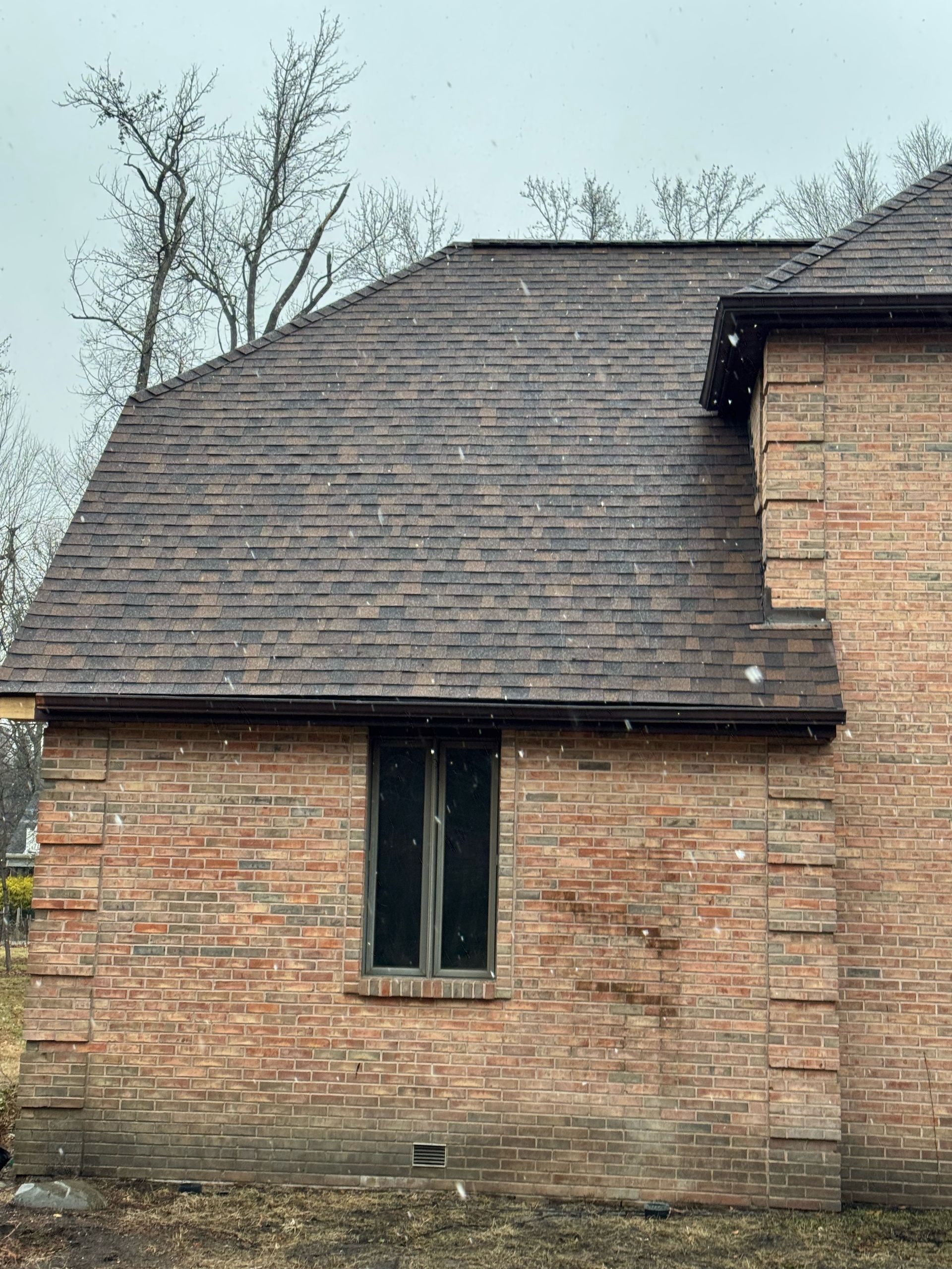 Brick building with a dark shingled roof and narrow window, viewed from outside under cloudy skies