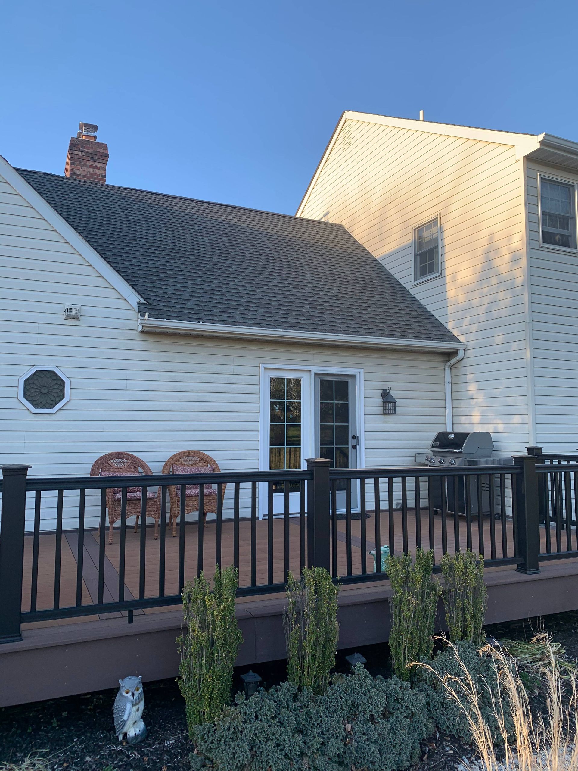 White house exterior with gray roof, brick chimney, black fence, and small landscaped shrubs.