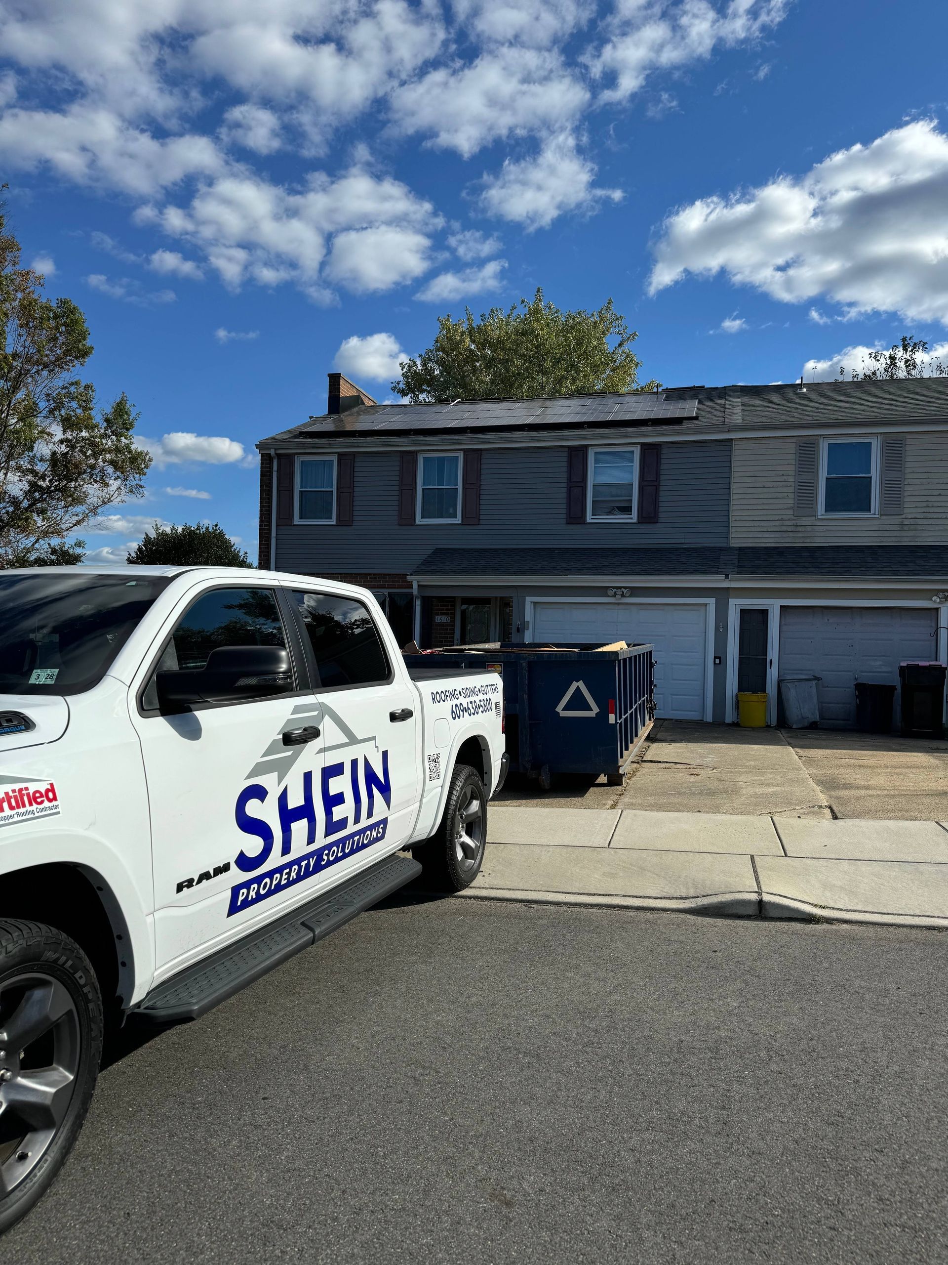 White Shein service truck parked beside a gray two-story townhouse under a blue, cloudy sky.