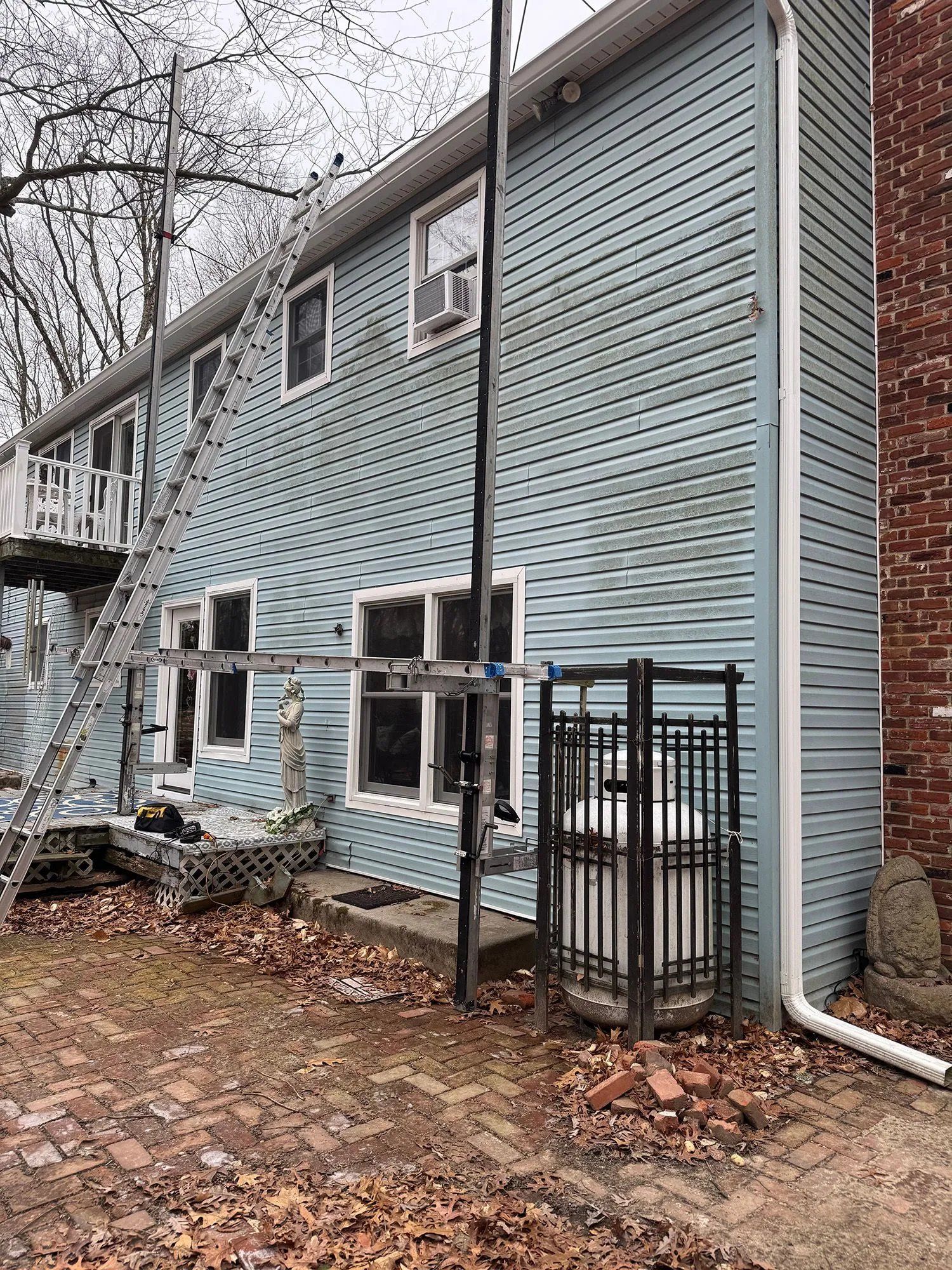 Two-story blue house exterior with ladder, broken lower windows, and fallen leaves in yard