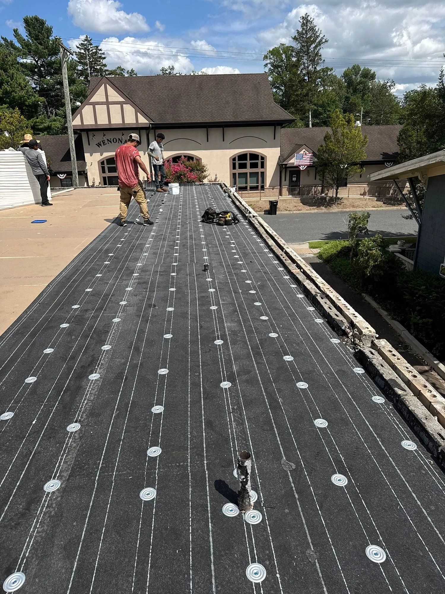 Roof being covered with black underlayment, with two workers on top near a Tudor-style house.