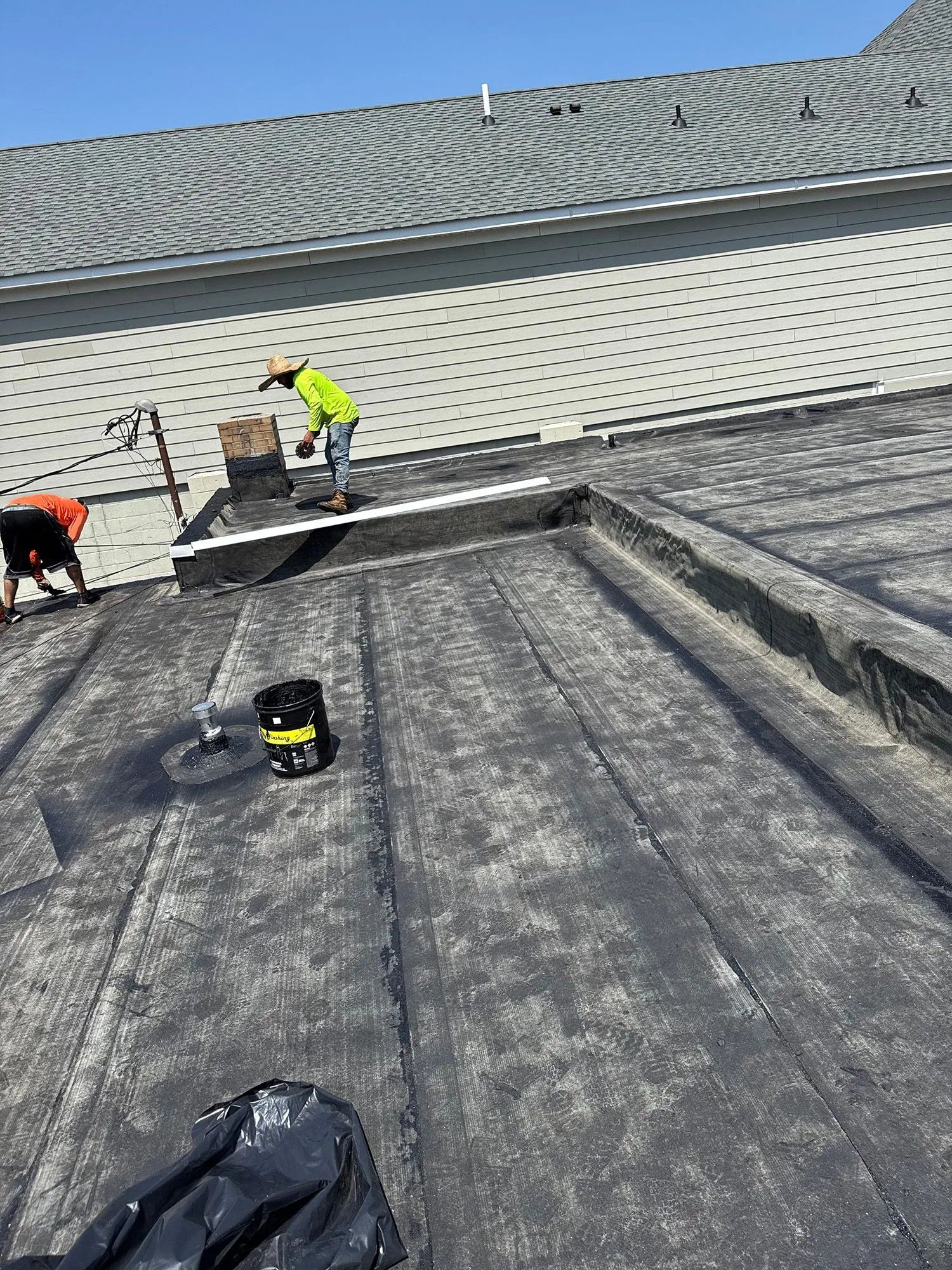 Workers repairing a rooftop with roofing materials on a sloped gray roof