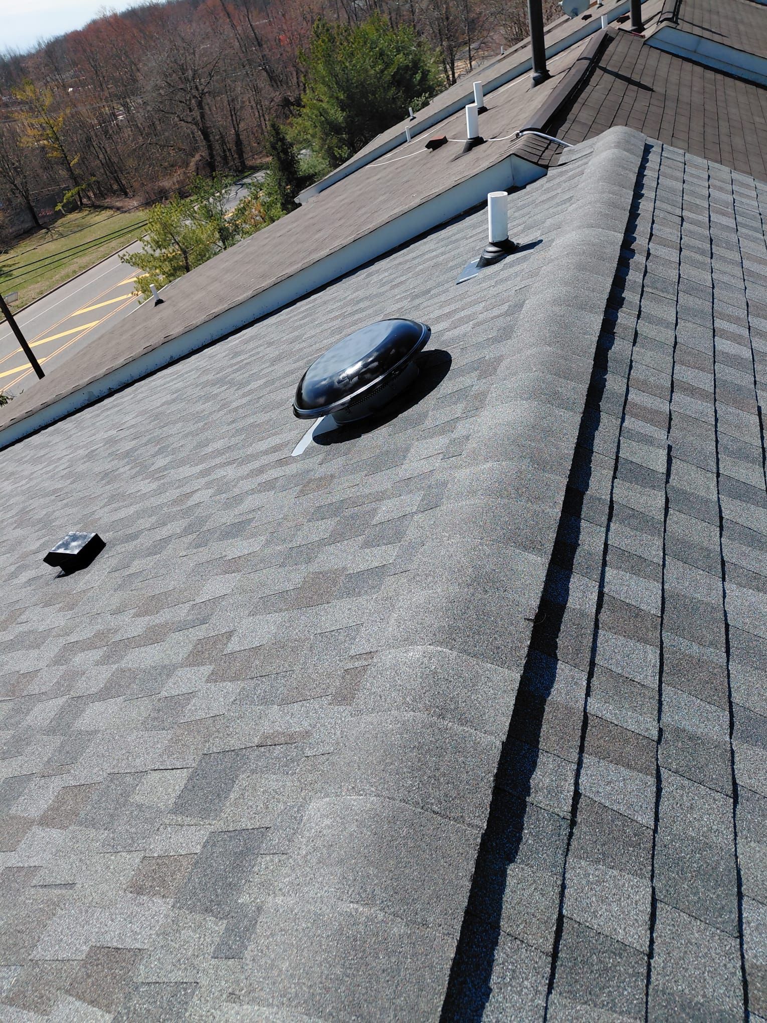 Roof with gray shingles, a black vent, and a vent pipe under a bright sky.
