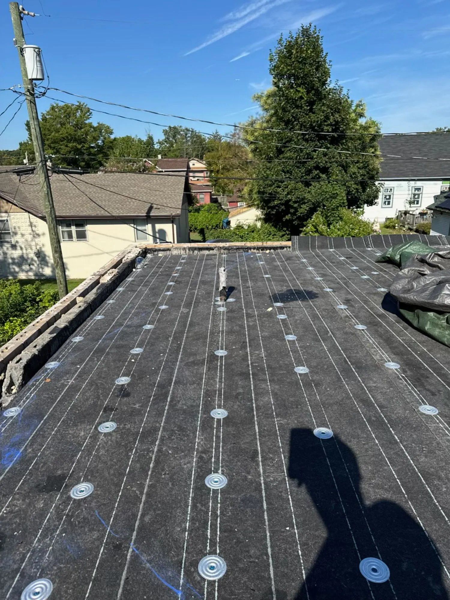 Flat rooftop with black underlayment, circular fasteners, and a sunny residential neighborhood in the background