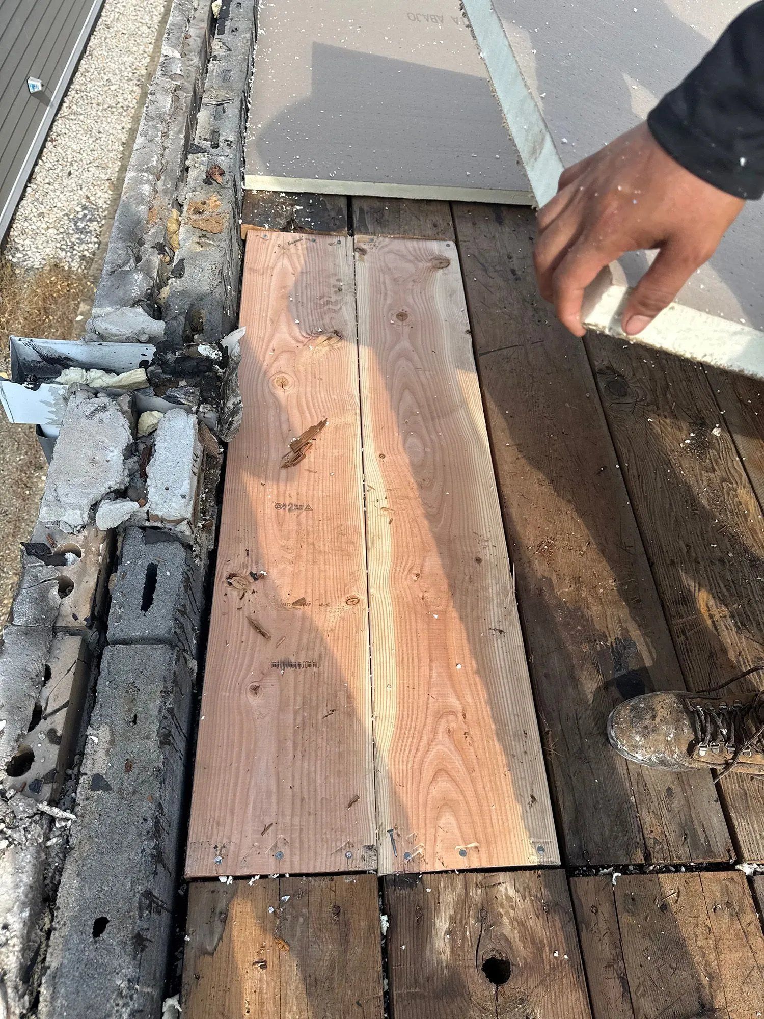 Wooden roof planks with a hand inspecting a damaged section near the edge of a roof.