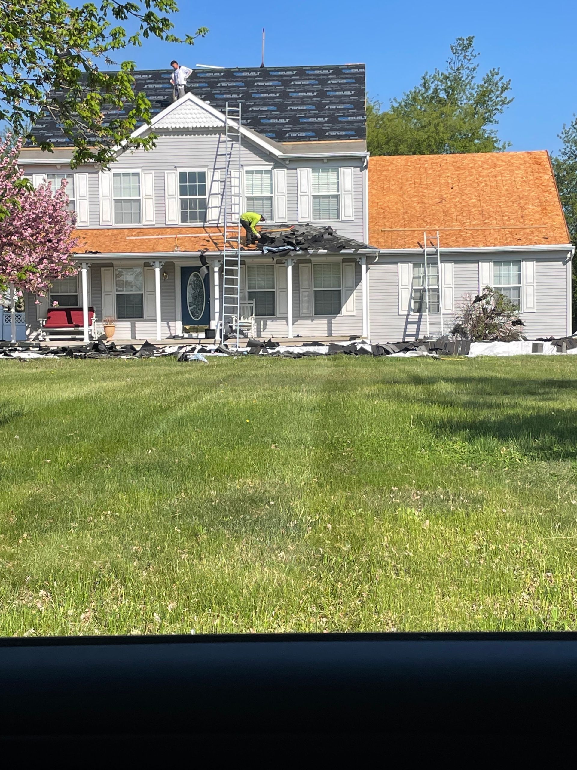 White two-story house with orange roof, porch, and green lawn under a clear blue sky