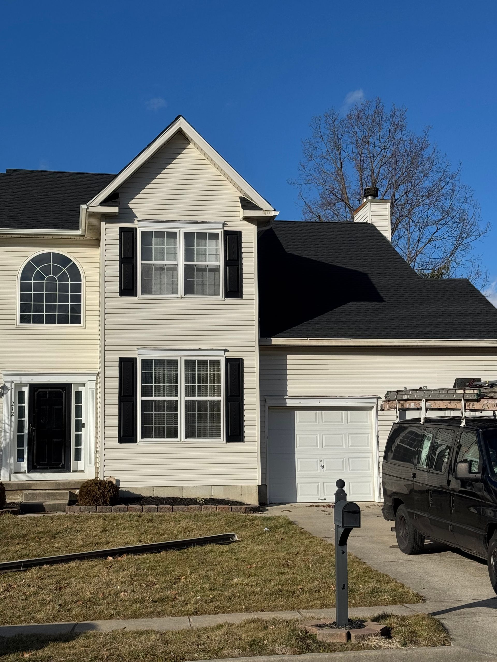 Two-story beige house with black shutters, attached garage, and a black SUV in the driveway