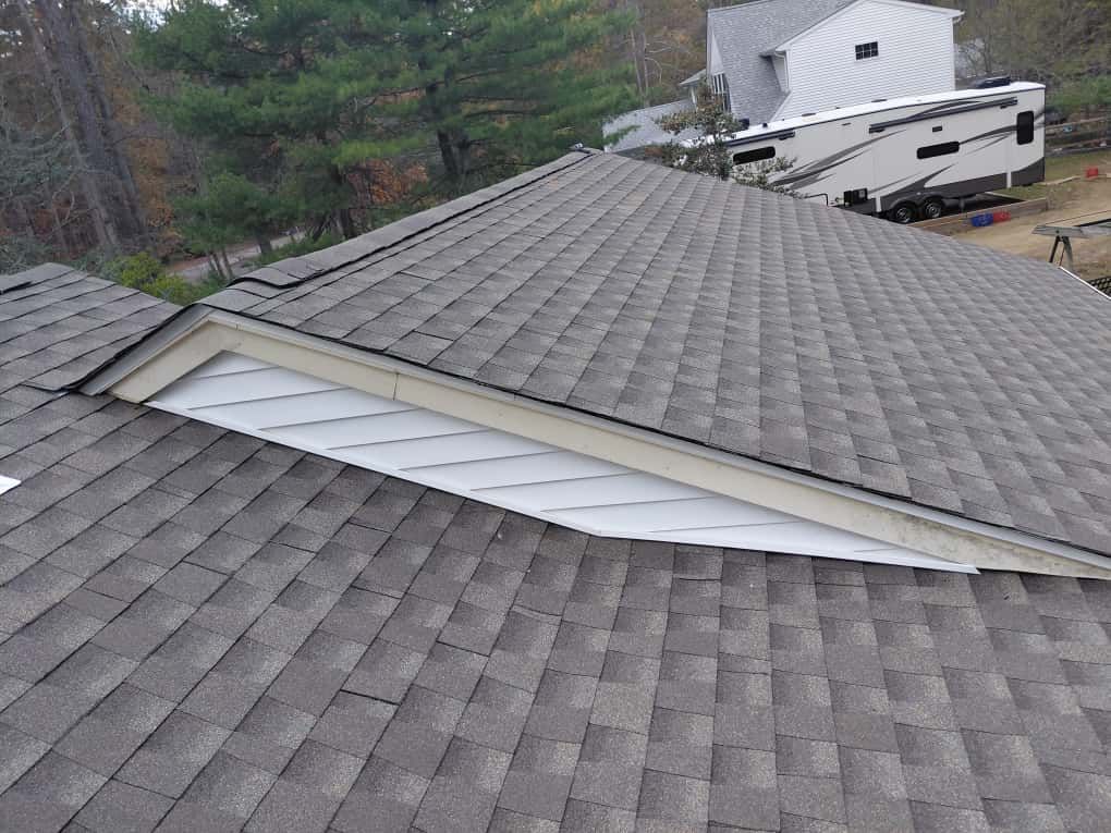 Damaged shingle roof with a long tear exposing white underlayment and a trailer in the background