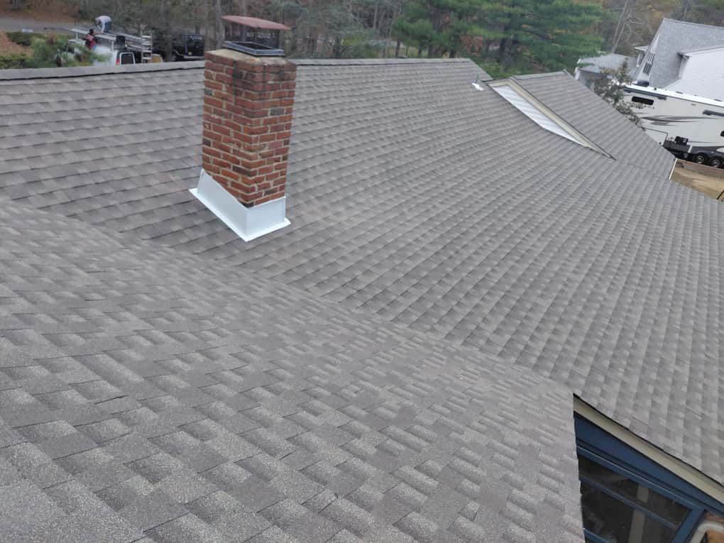 Gray shingled roof with a brick chimney and roof vent in a suburban neighborhood