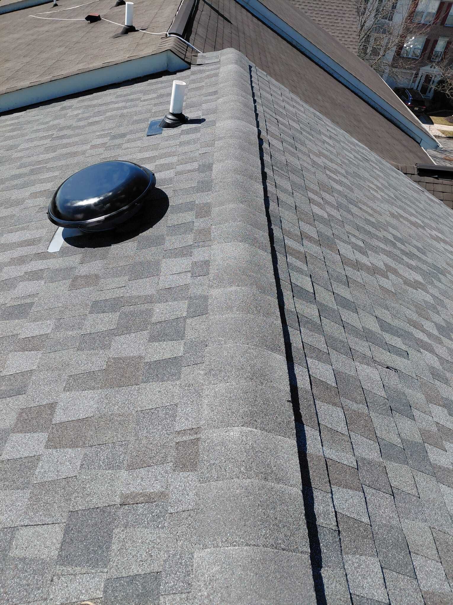 Roof shingles with a black vent pipe and a white vent on a steep sloped rooftop.