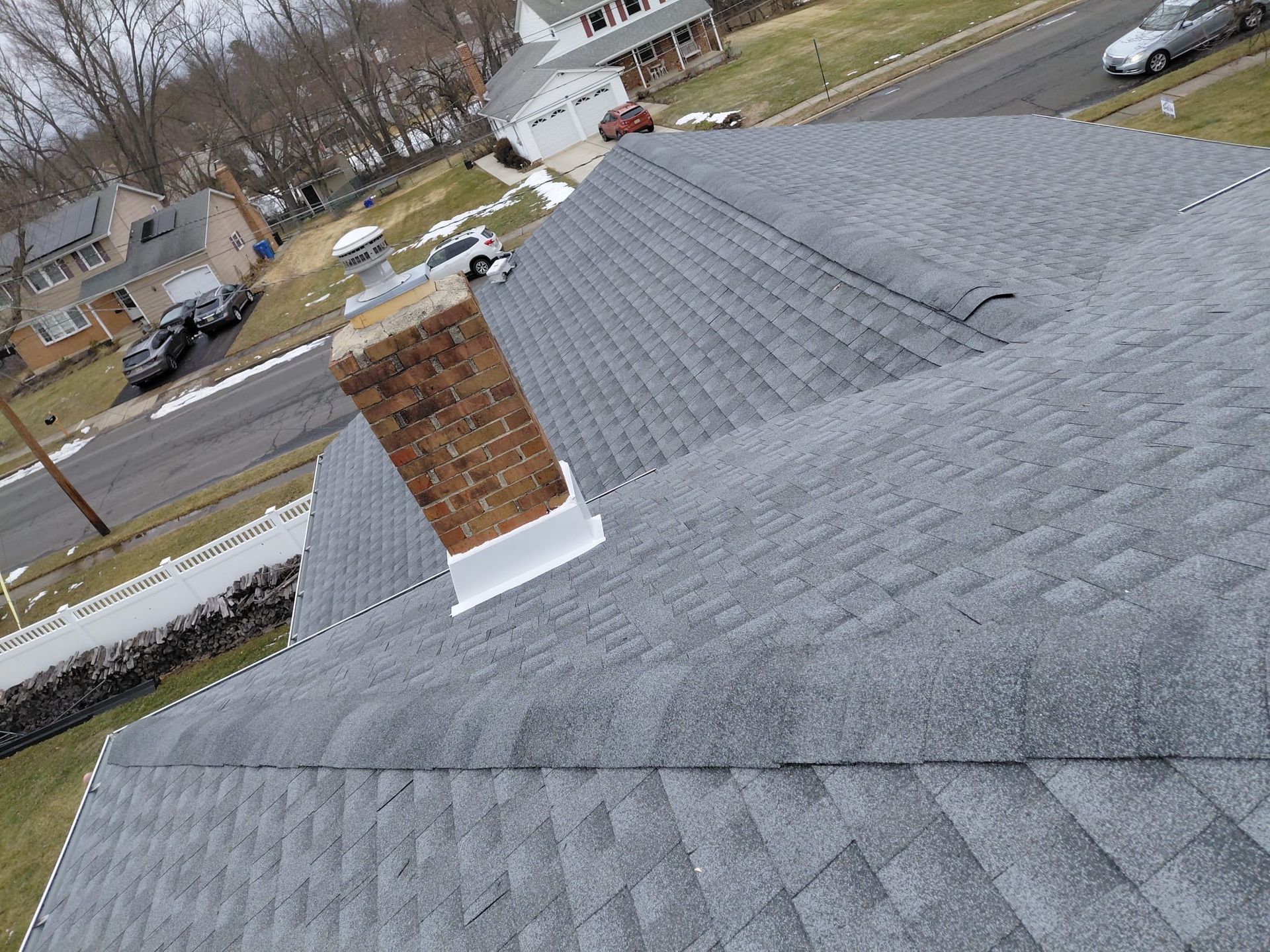 Gray shingled roof with a brick chimney, viewed from above near a suburban street