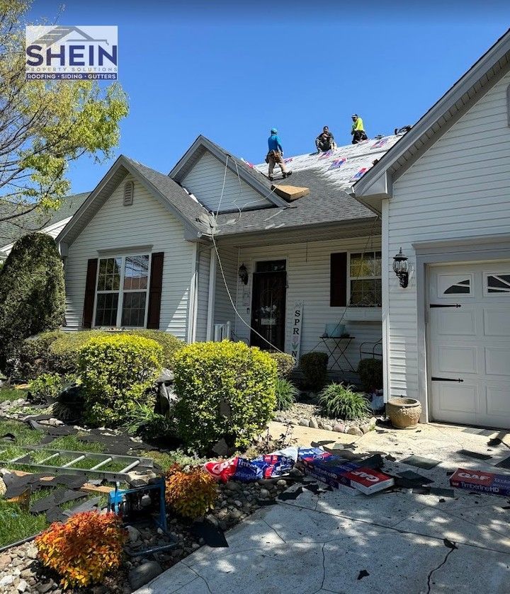 Workers repairing a house roof with shingles and tools on the front lawn