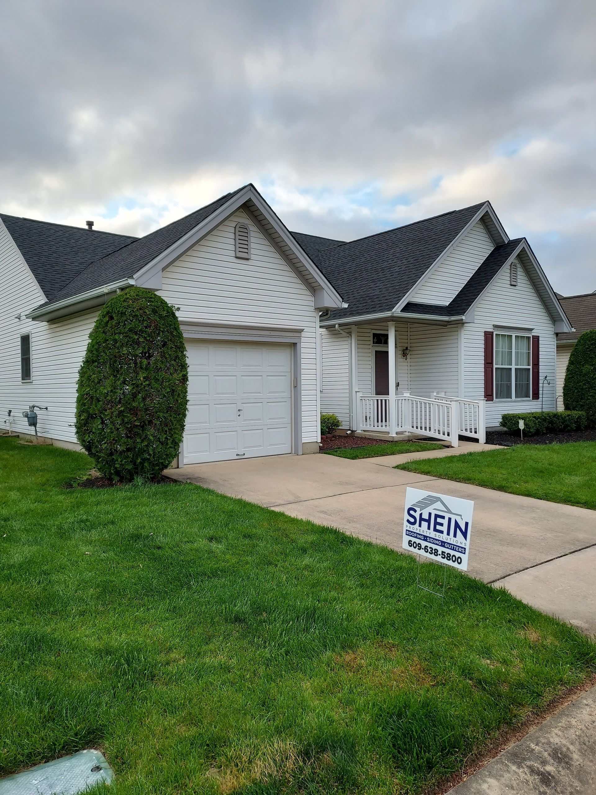 Suburban house with white siding, dark roof, green lawn, and a small sign by the driveway