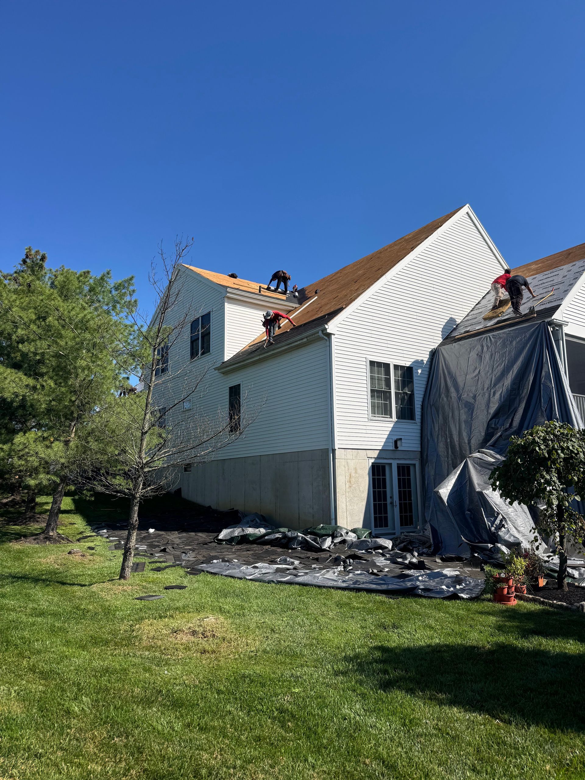 Two-story white house with orange roof under repair, with workers on the roof and a grassy yard in front