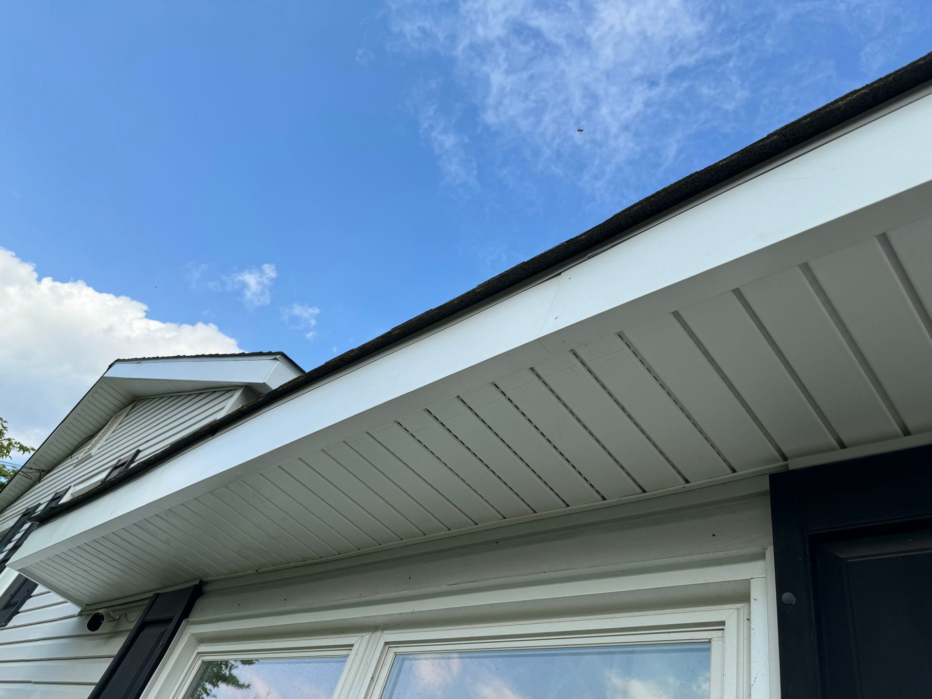 Close-up of a white house eave and soffit under a blue sky, with a dark trim roof edge.