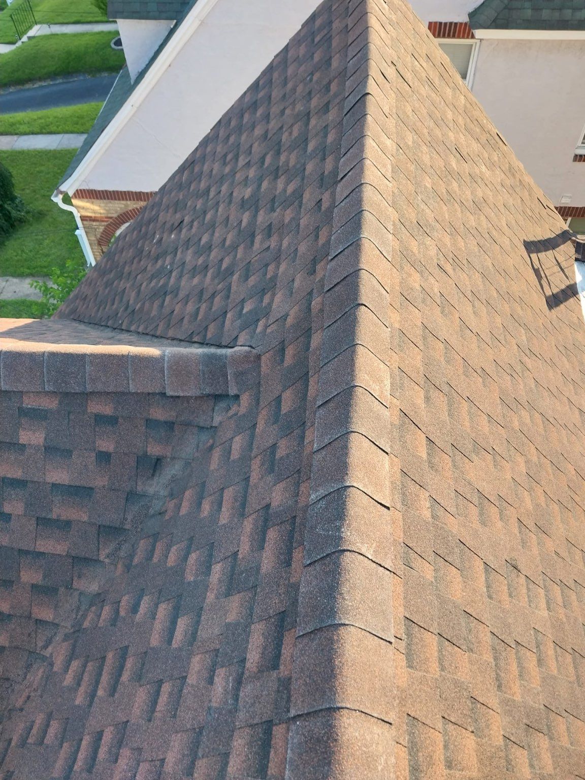 Aerial view of a brown shingled roof with a steep ridge and triangular dormer.