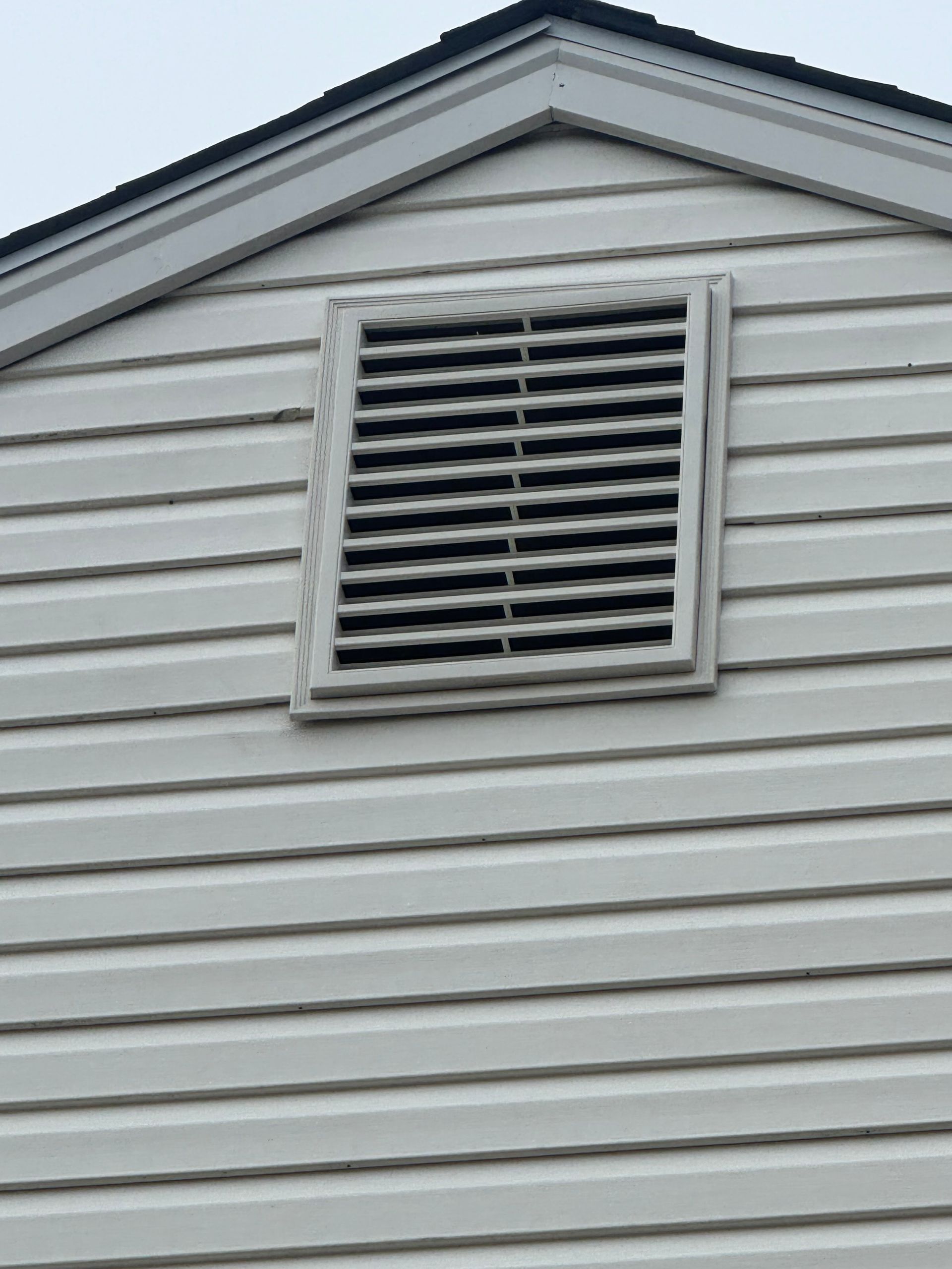 White house siding with a small louvered vent near the roof peak