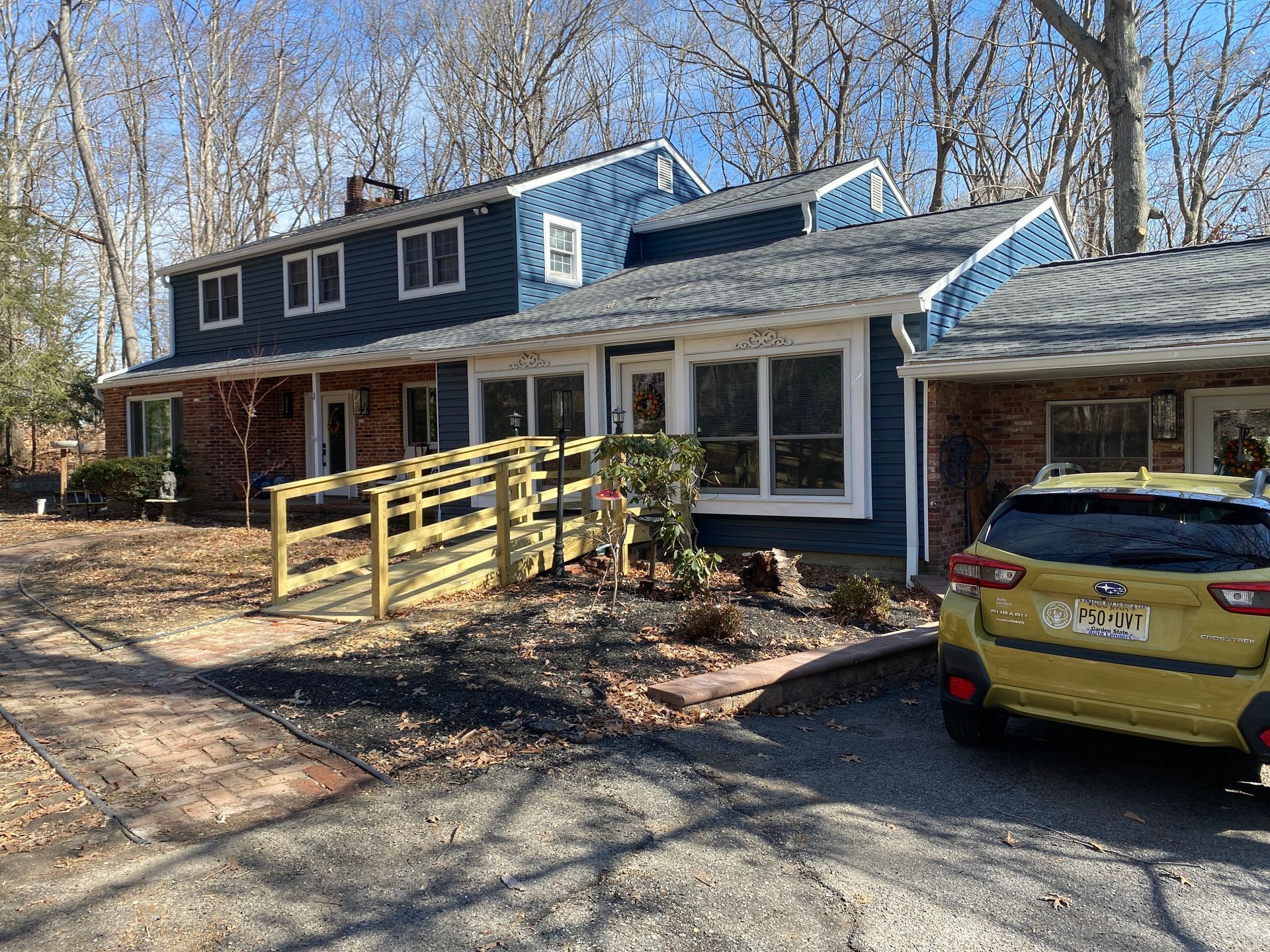 Suburban house with blue siding, yellow ramp, and yellow car parked in front under bare trees