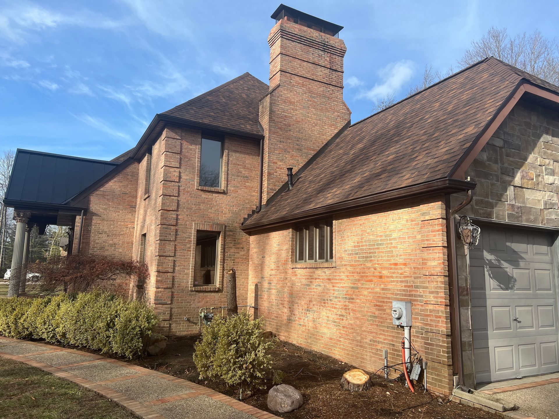 Brick house exterior with sloped roof, chimney, and attached garage on a sunny day