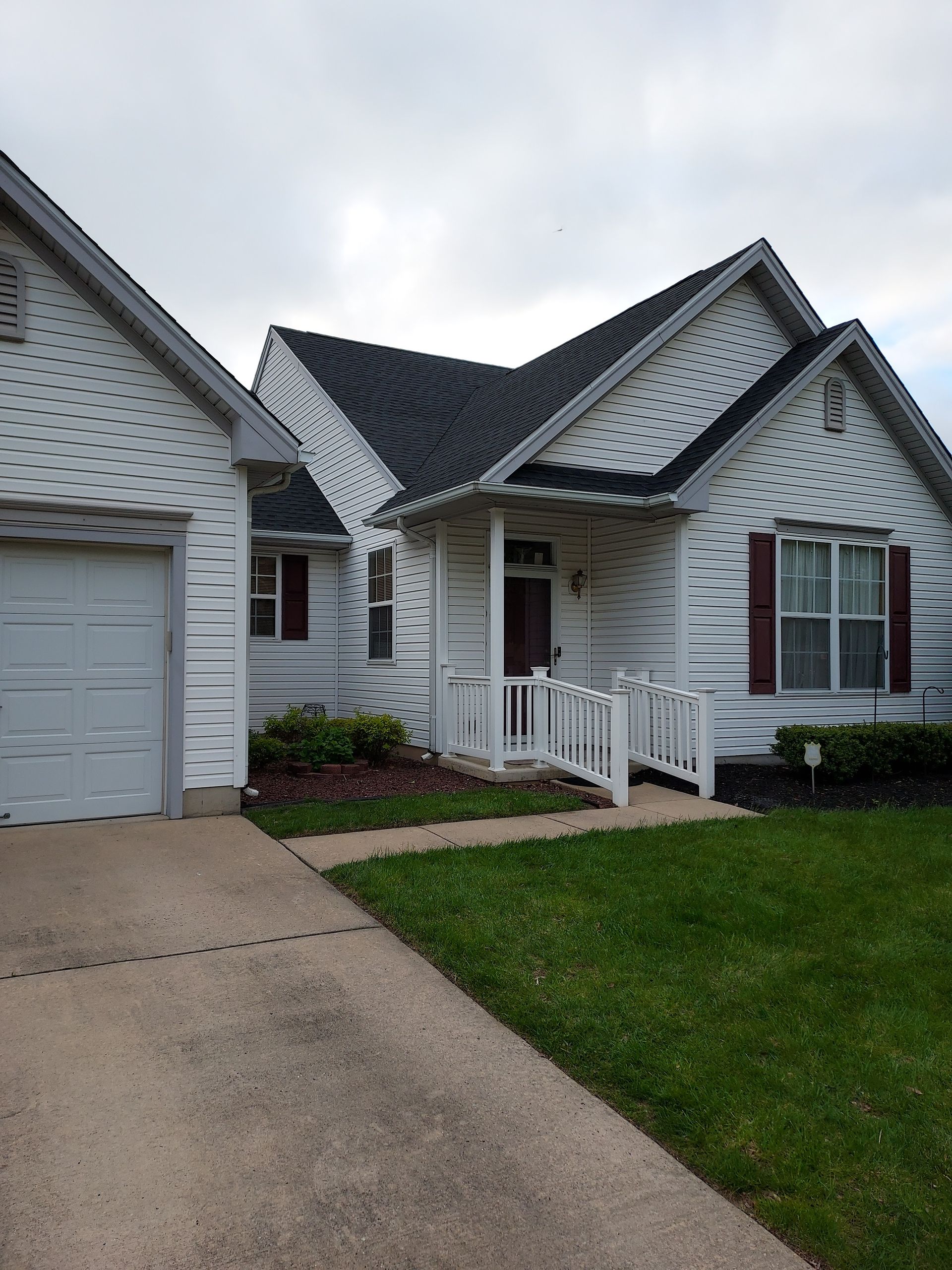 White house with attached garage, front porch, and concrete driveway, seen from the front-yard lawn