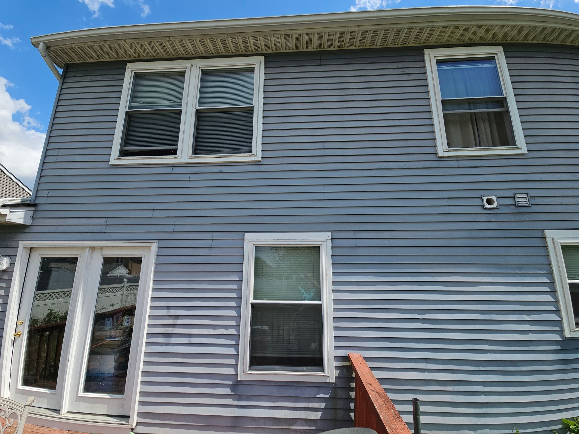 Blue-gray house exterior with white-trim windows, a glass door, and a small stair railing under a blue sky