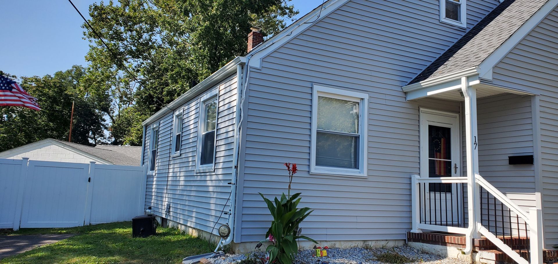 Blue-gray house exterior with white trim, porch, and side yard fenced with a white gate