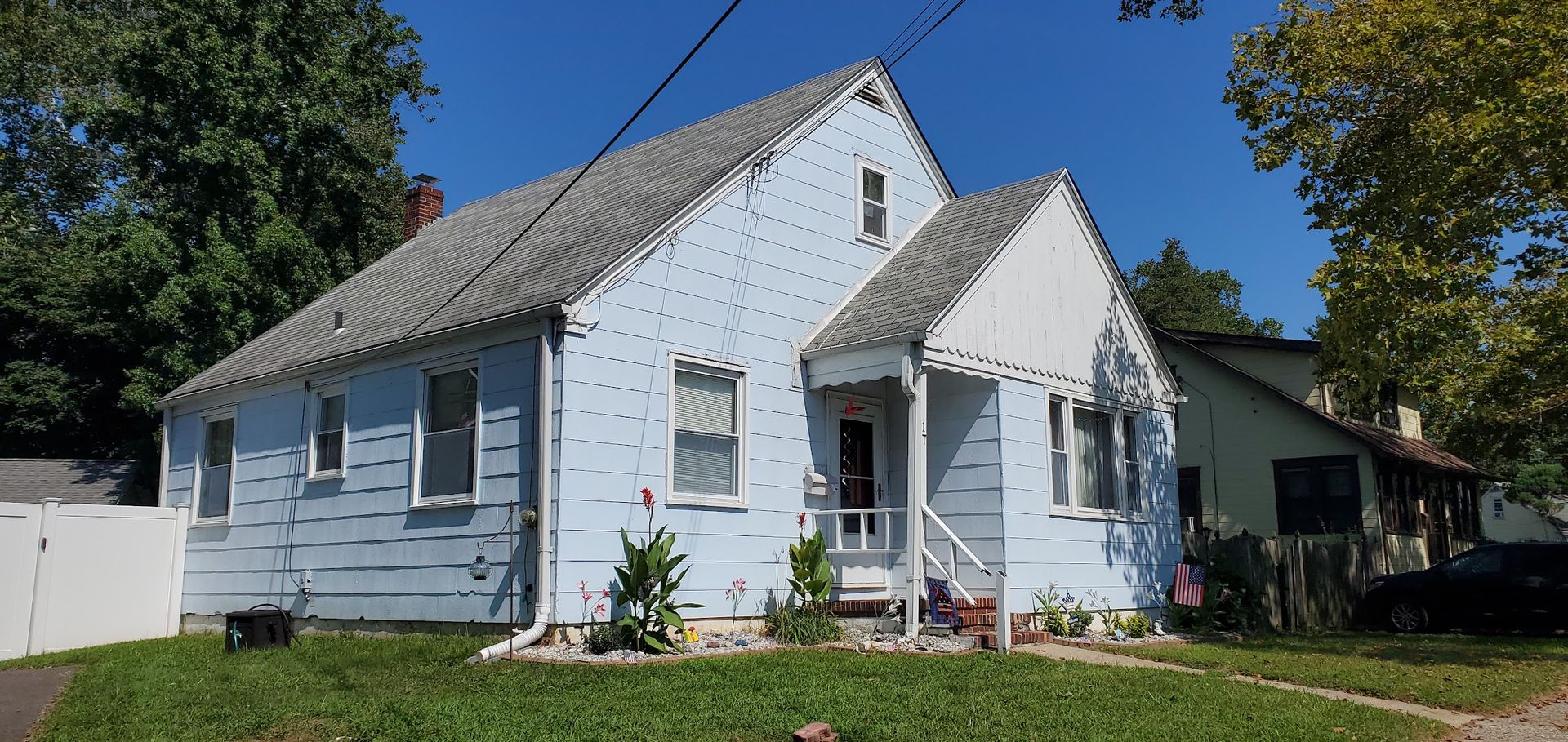 White house with a steep roof, small porch, and front garden on a sunny day