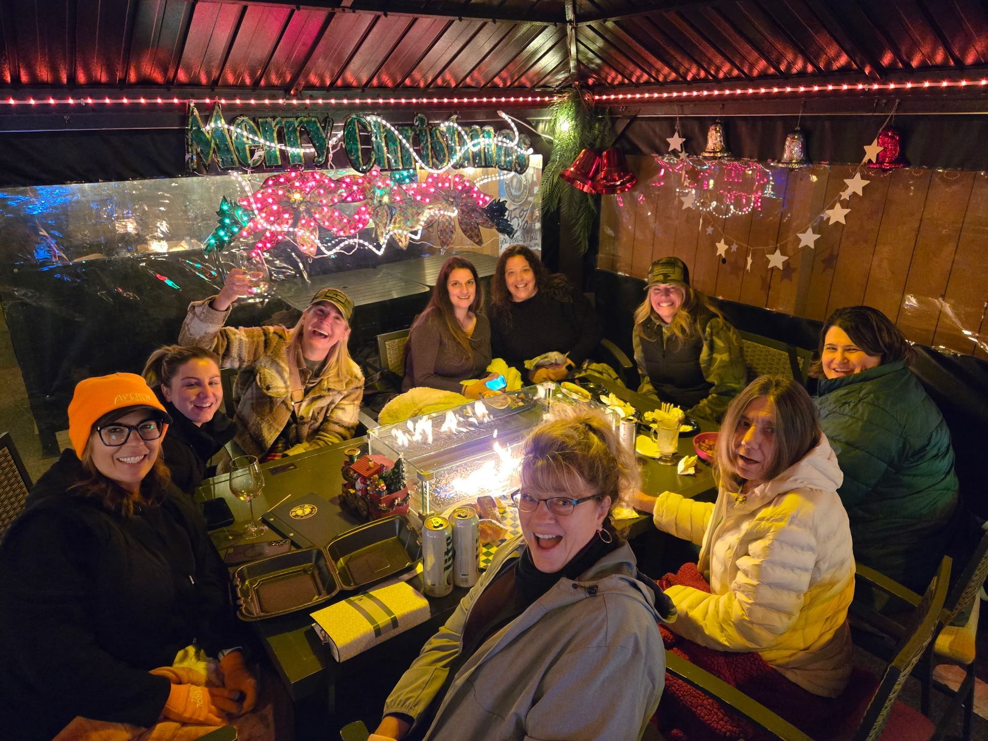 Group of people gathered around a fire pit in a decorated outdoor area, smiling and interacting.
