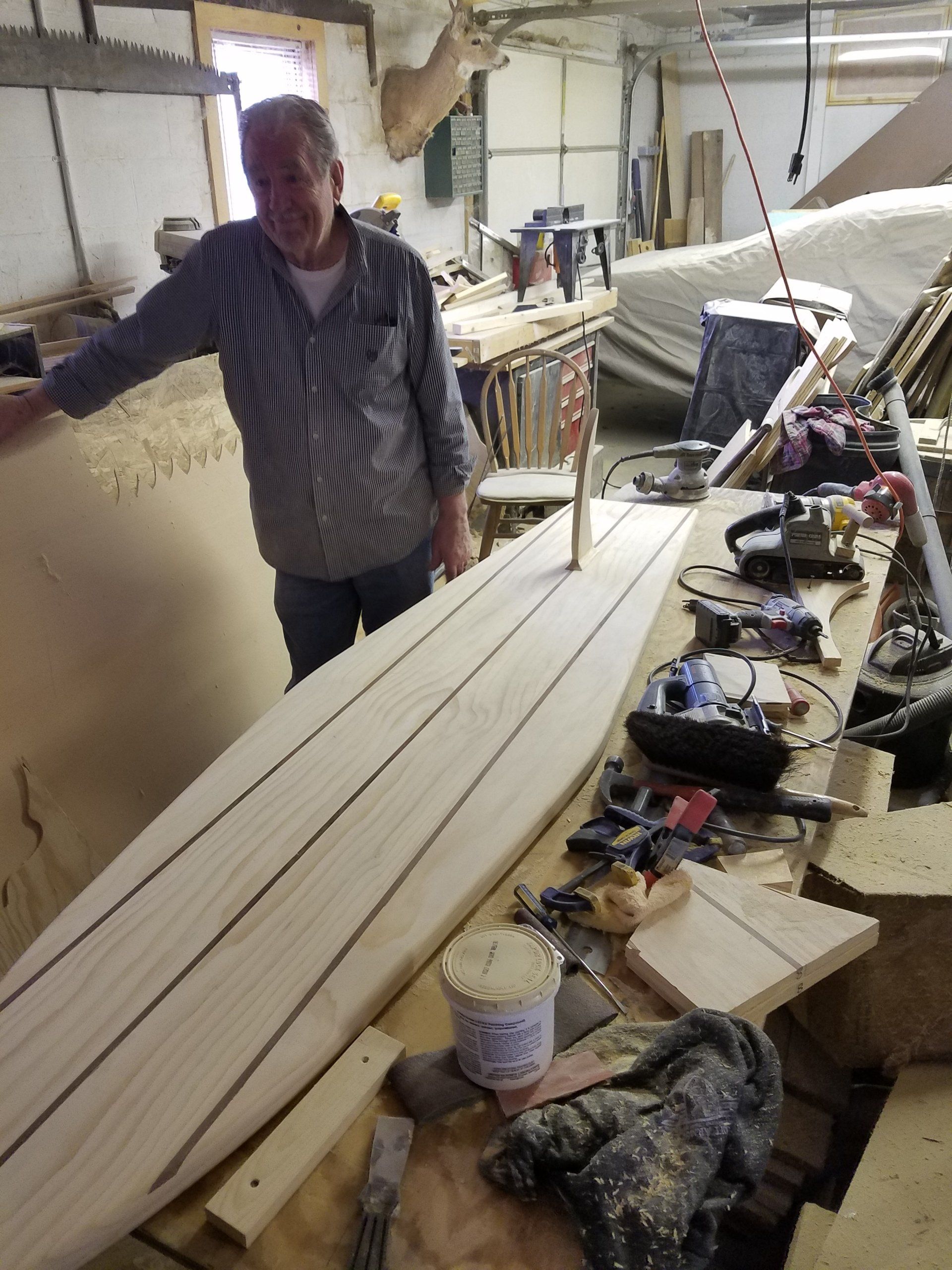 A man standing next to a wooden surfboard in a workshop